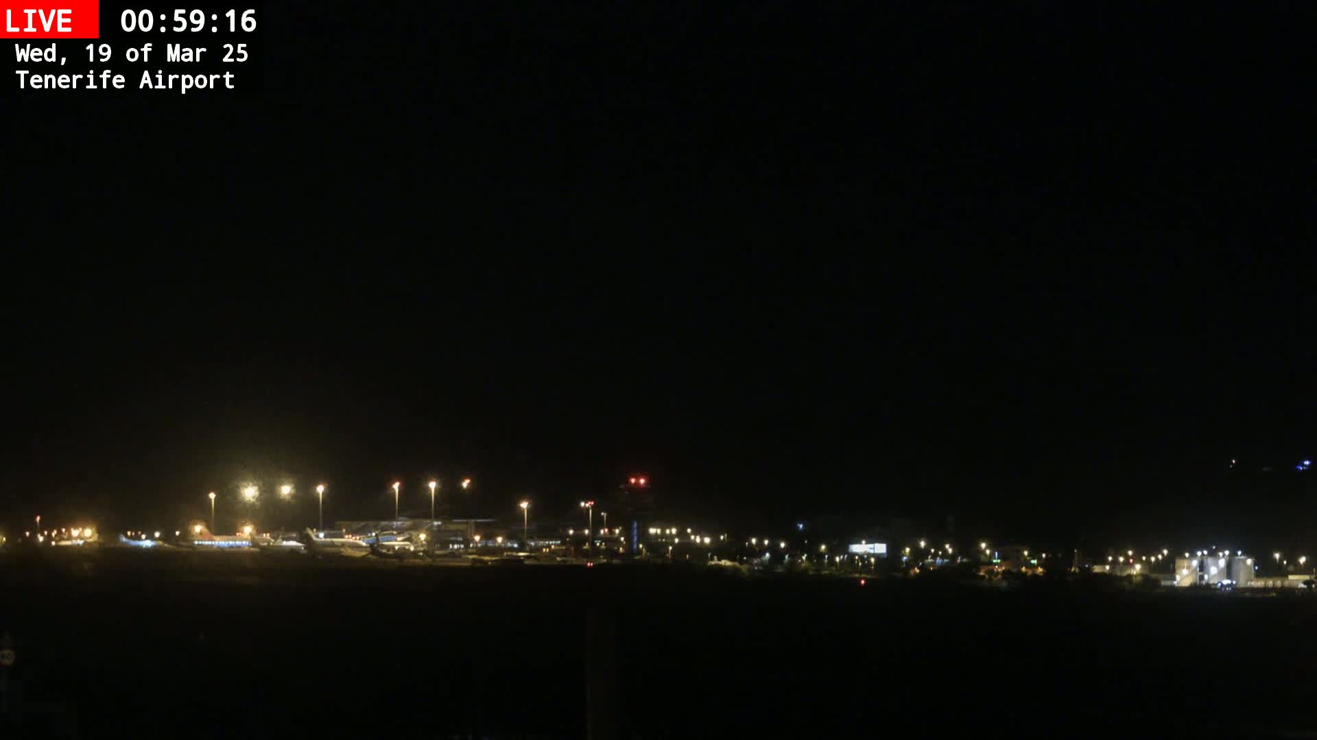 A nighttime long shot of an airport with its lights illuminating the tarmac and surrounding area under a clear, dark sky.
