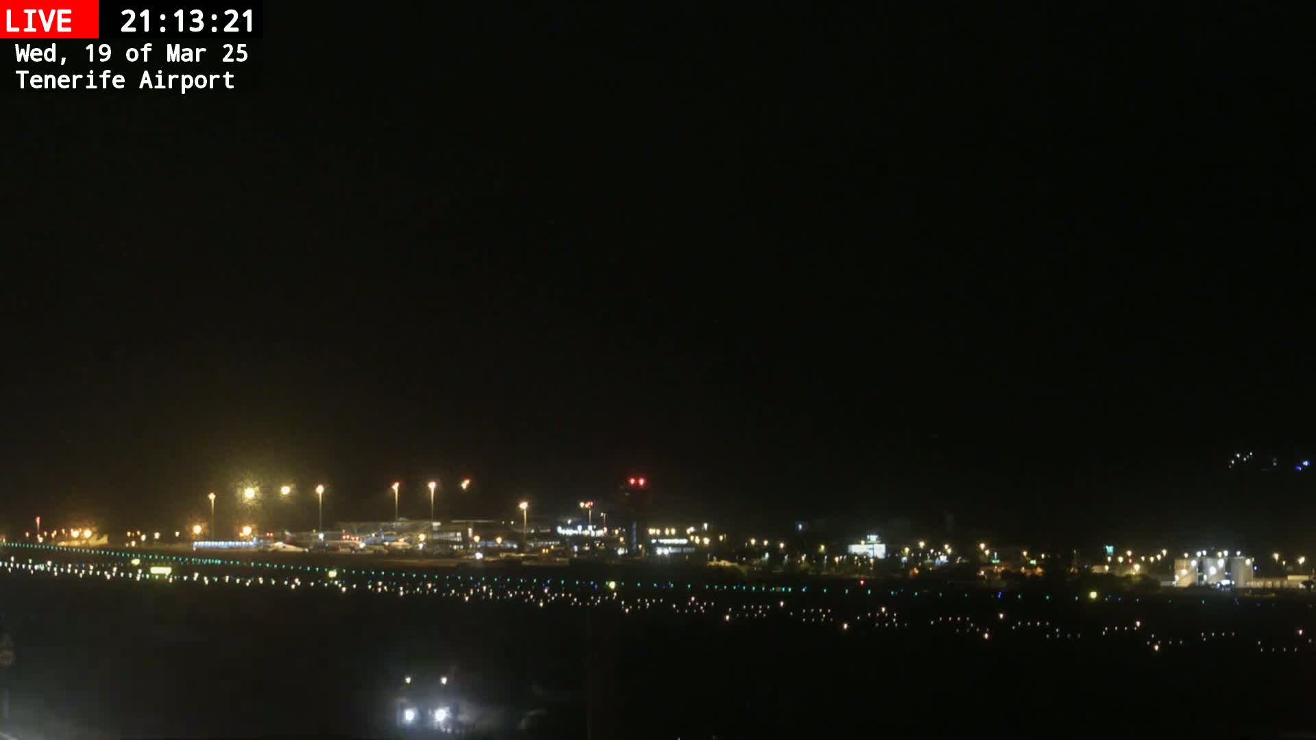 A nighttime long shot of an airport runway with its lights illuminated under a clear, dark sky.