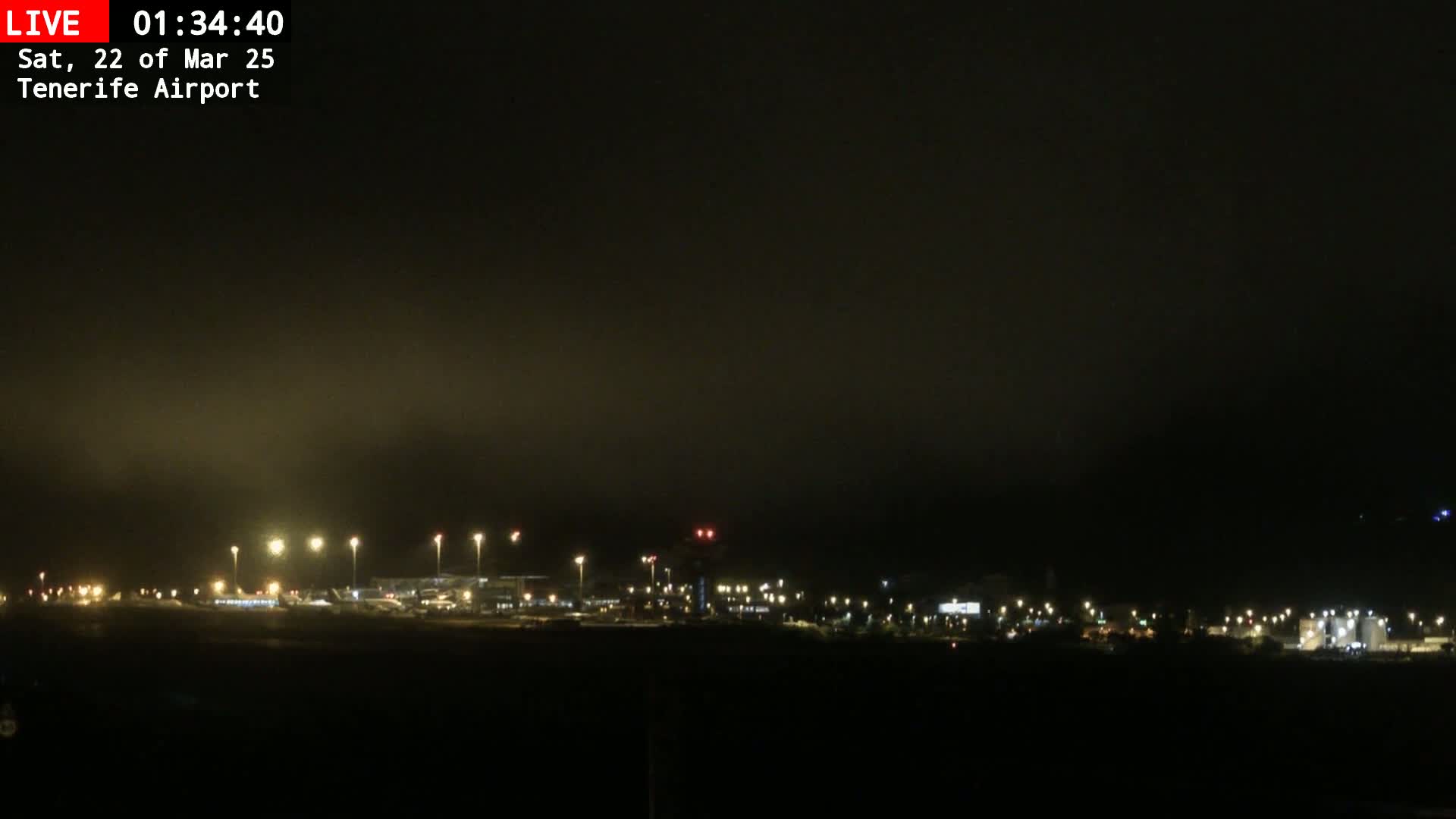 A nighttime view of an airport runway and terminal buildings under a foggy sky.