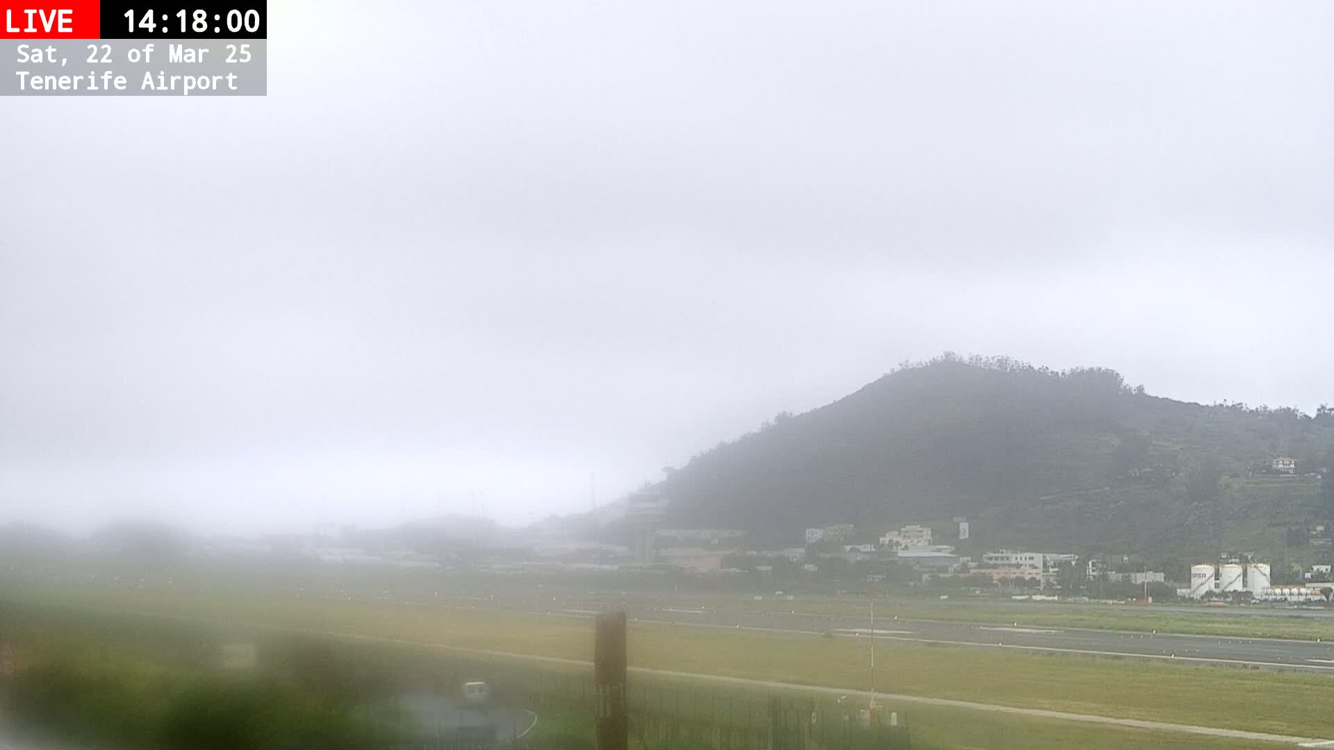A foggy view of an airport runway and a hill in the background.