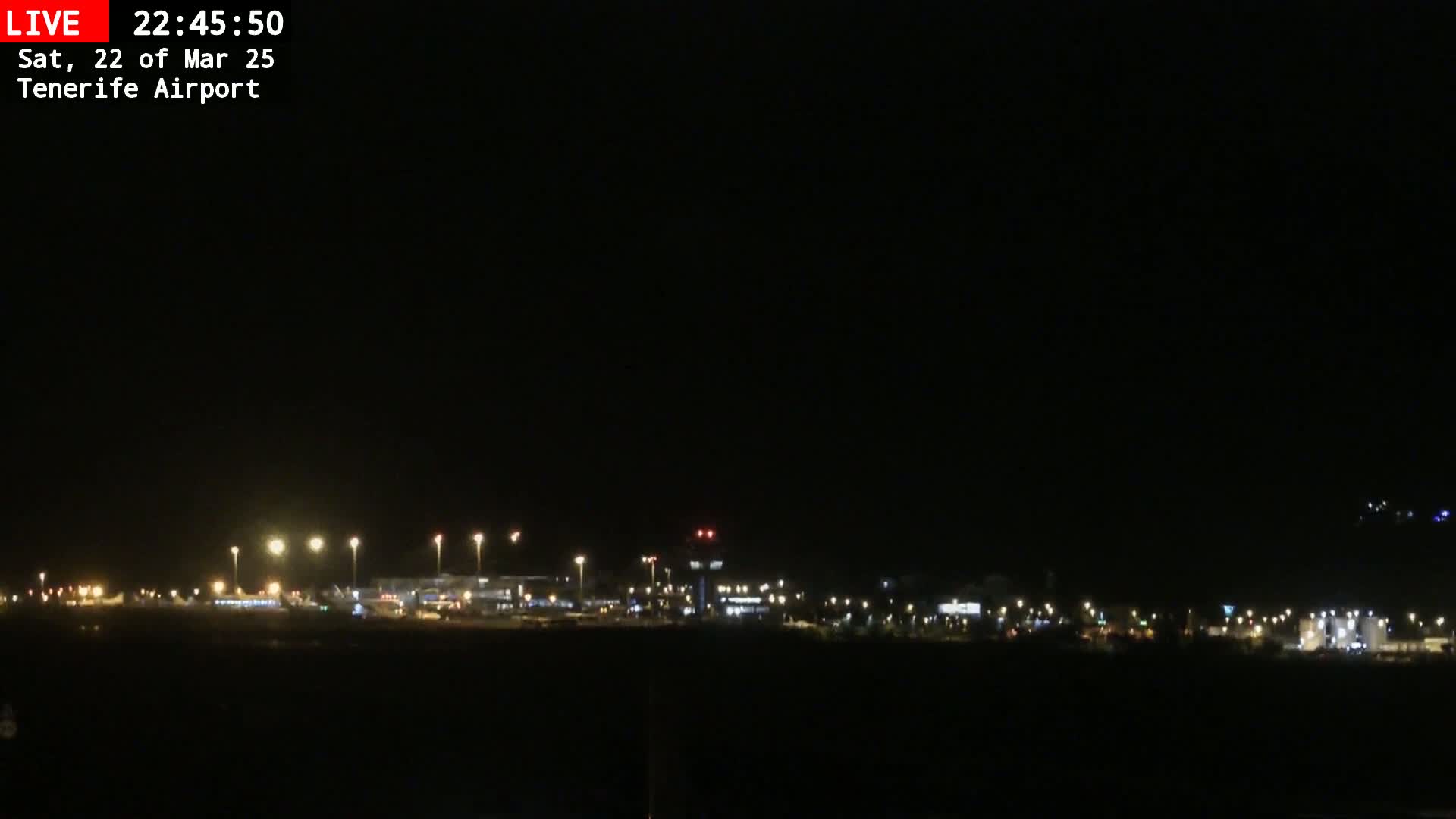 A nighttime view of an airport with its lights illuminating the tarmac and surrounding buildings under a dark, clear sky.