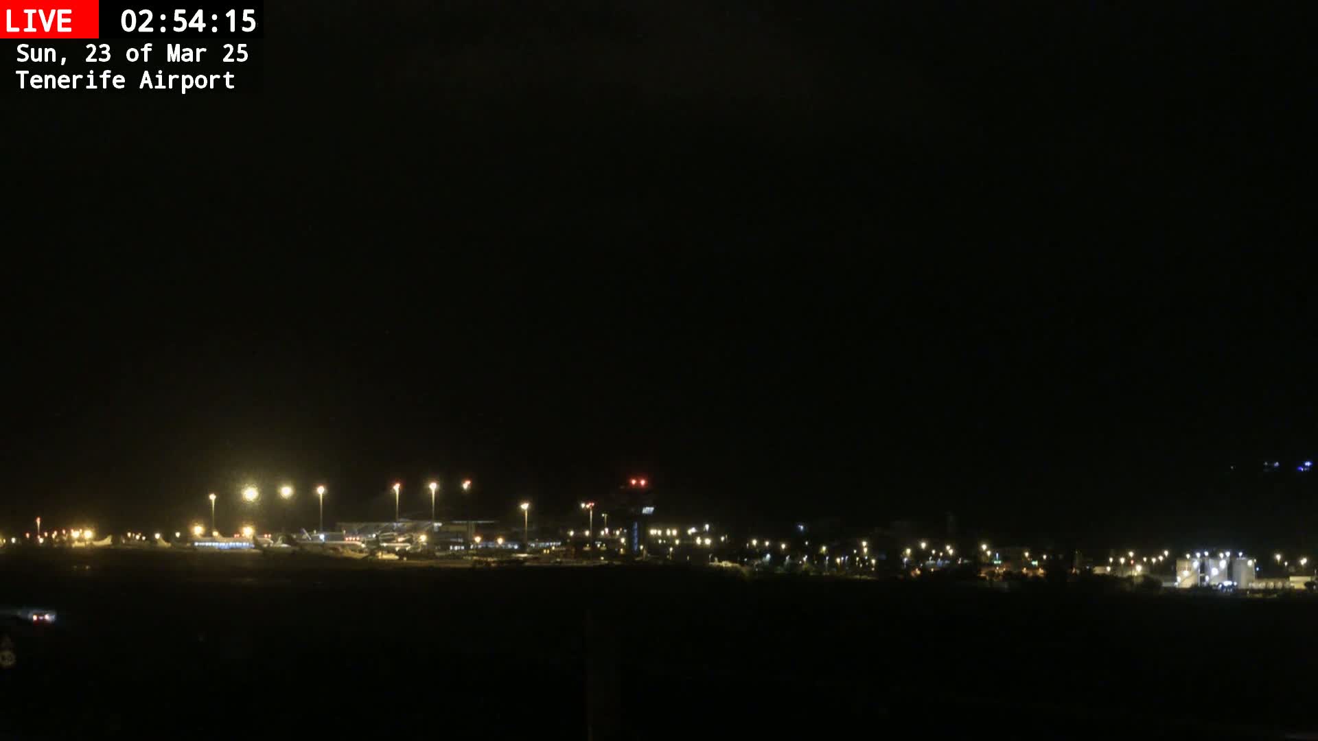 A nighttime view of an airport runway and terminal buildings illuminated by lights under a dark, clear sky.