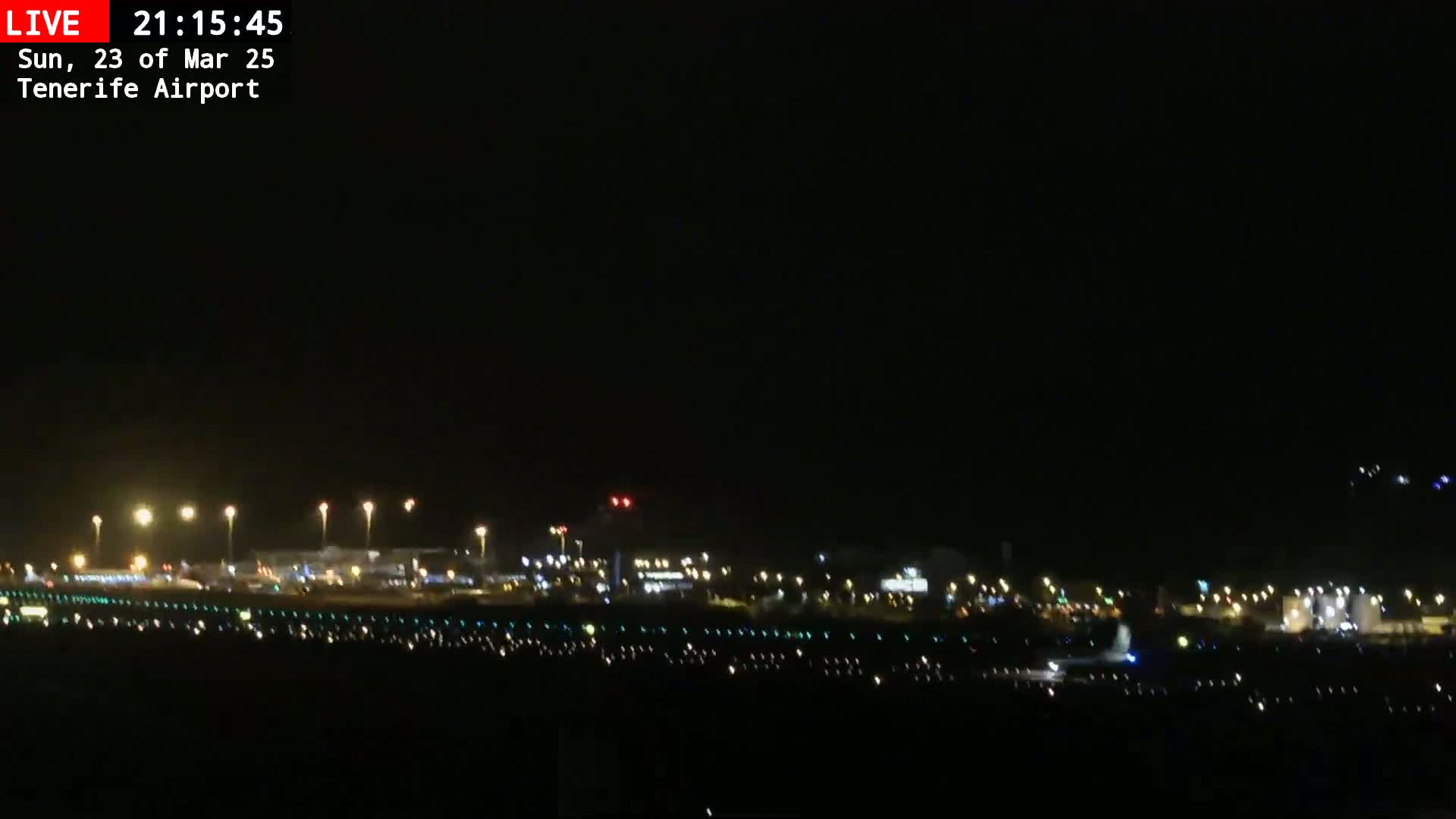 A nighttime view of an airport runway and terminal buildings illuminated by numerous lights under a clear, dark sky.