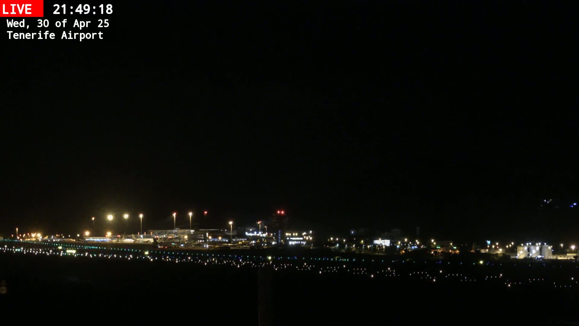 A nighttime long shot of an airport runway and terminal buildings illuminated under a clear, dark sky.