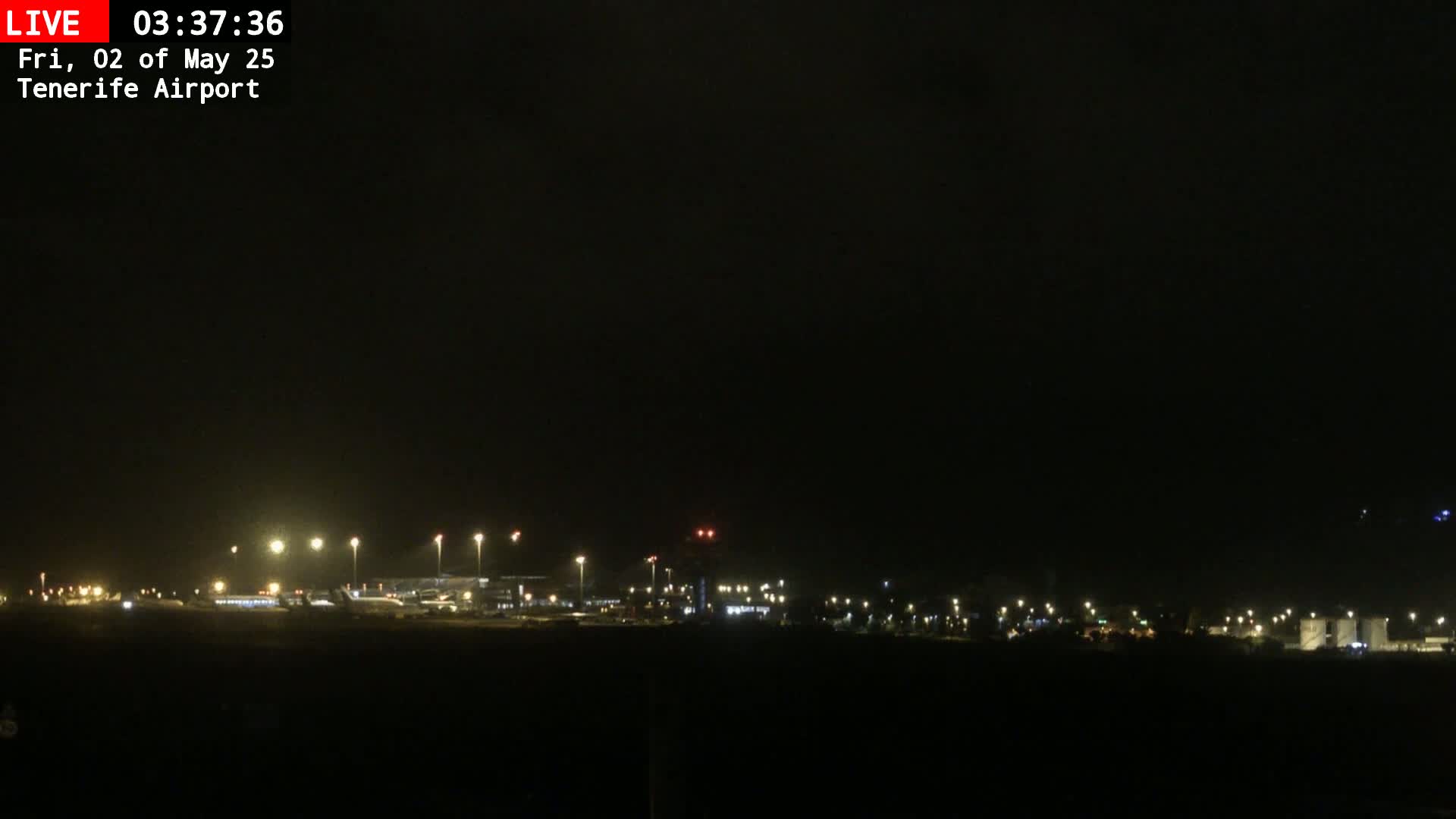 A dark, nighttime view of an airport runway and terminal buildings illuminated by artificial lights.