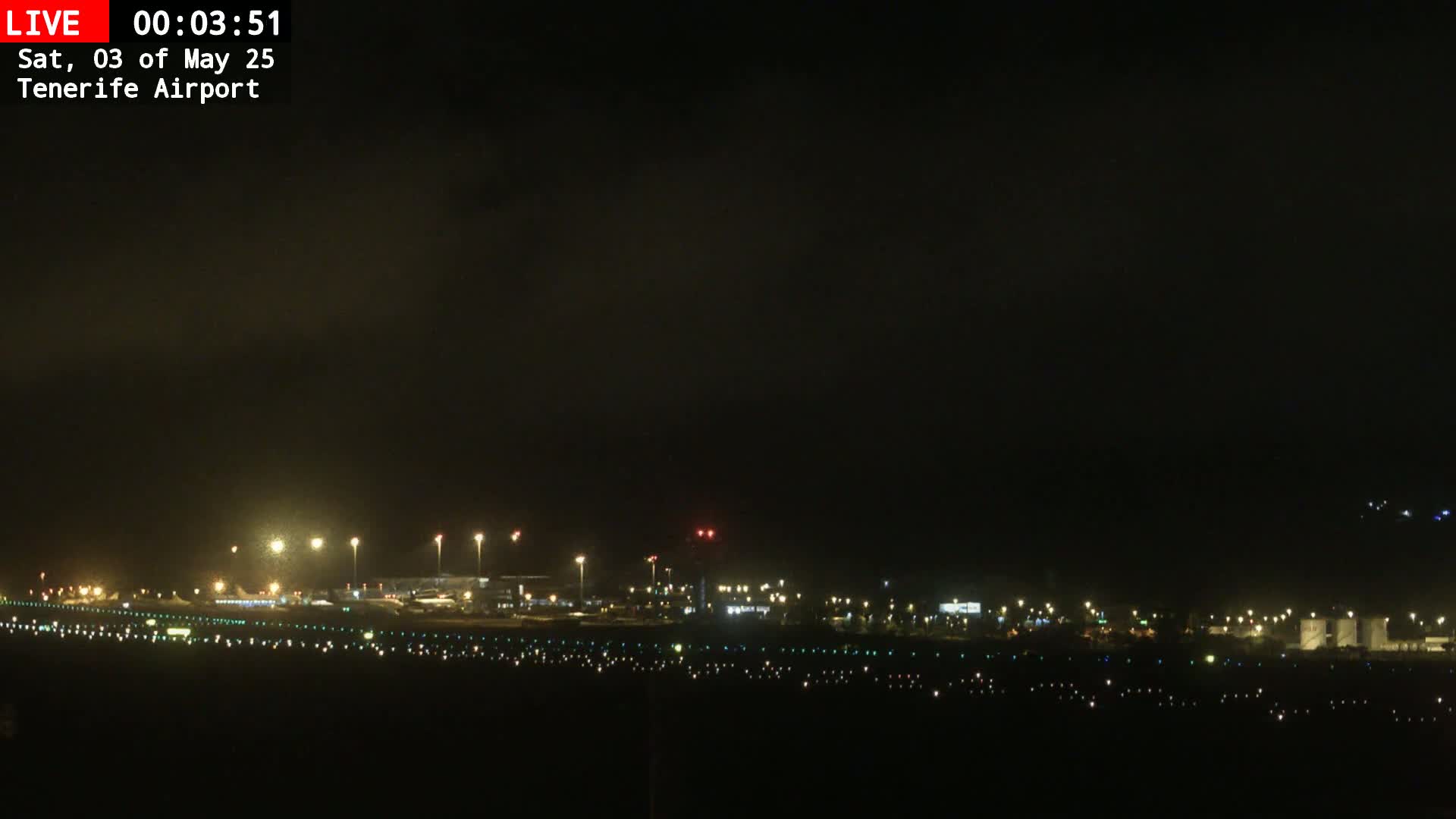 A nighttime, slightly hazy view of an airport runway and terminal buildings illuminated by lights.