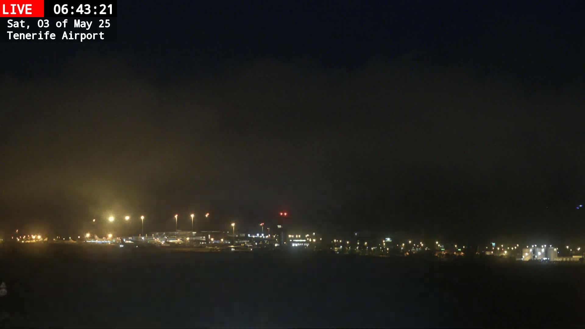 A nighttime view of an airport under hazy or foggy conditions, showing dimly lit buildings and runways.