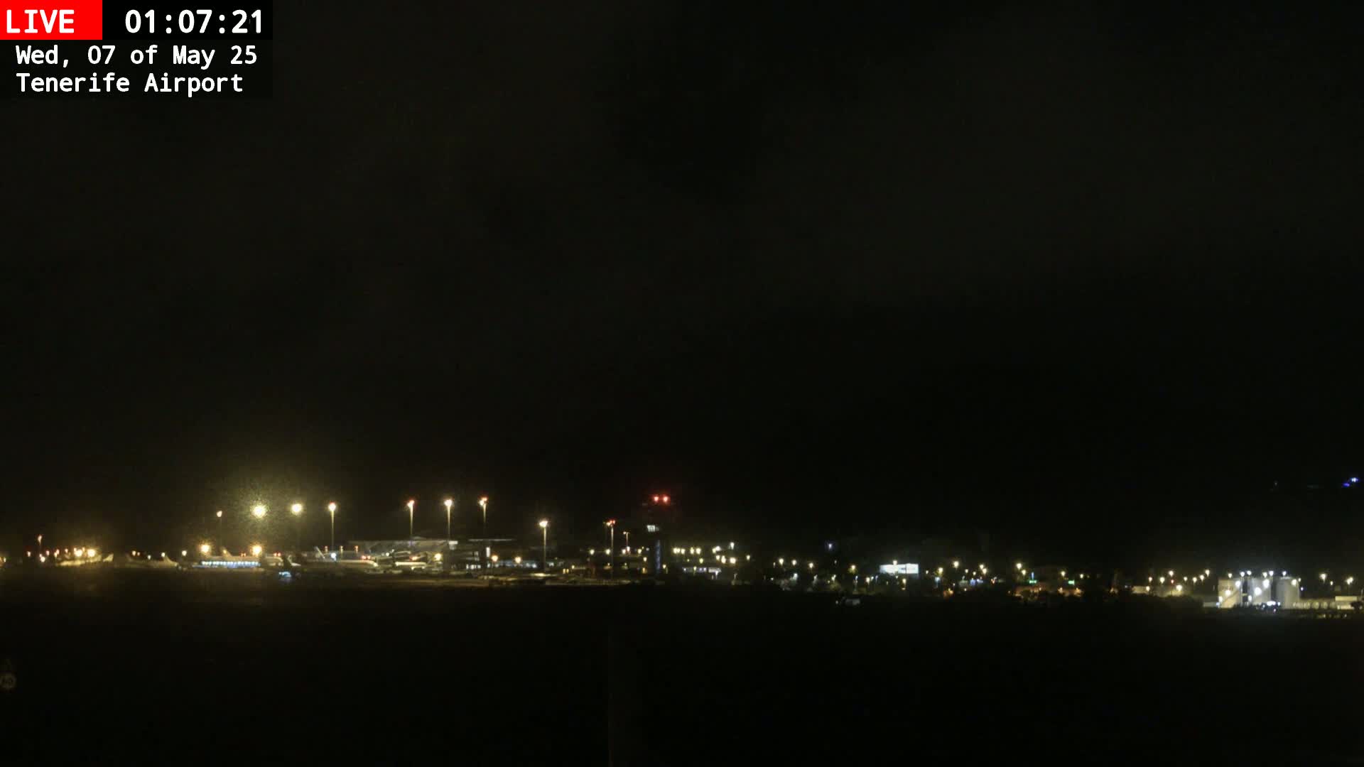 A nighttime view of an airport illuminated by numerous lights under a dark, cloudy sky.