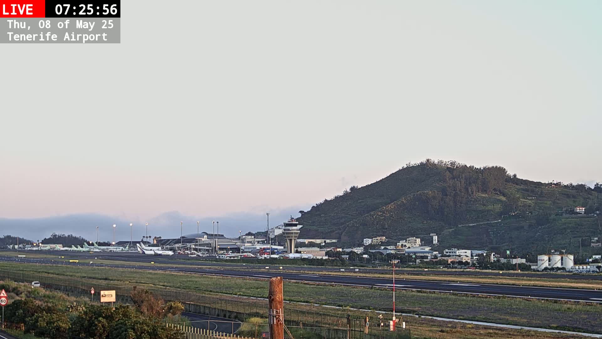 Several airplanes are parked on the tarmac of an airport, with a hill visible in the background under a pale, clear sky.
