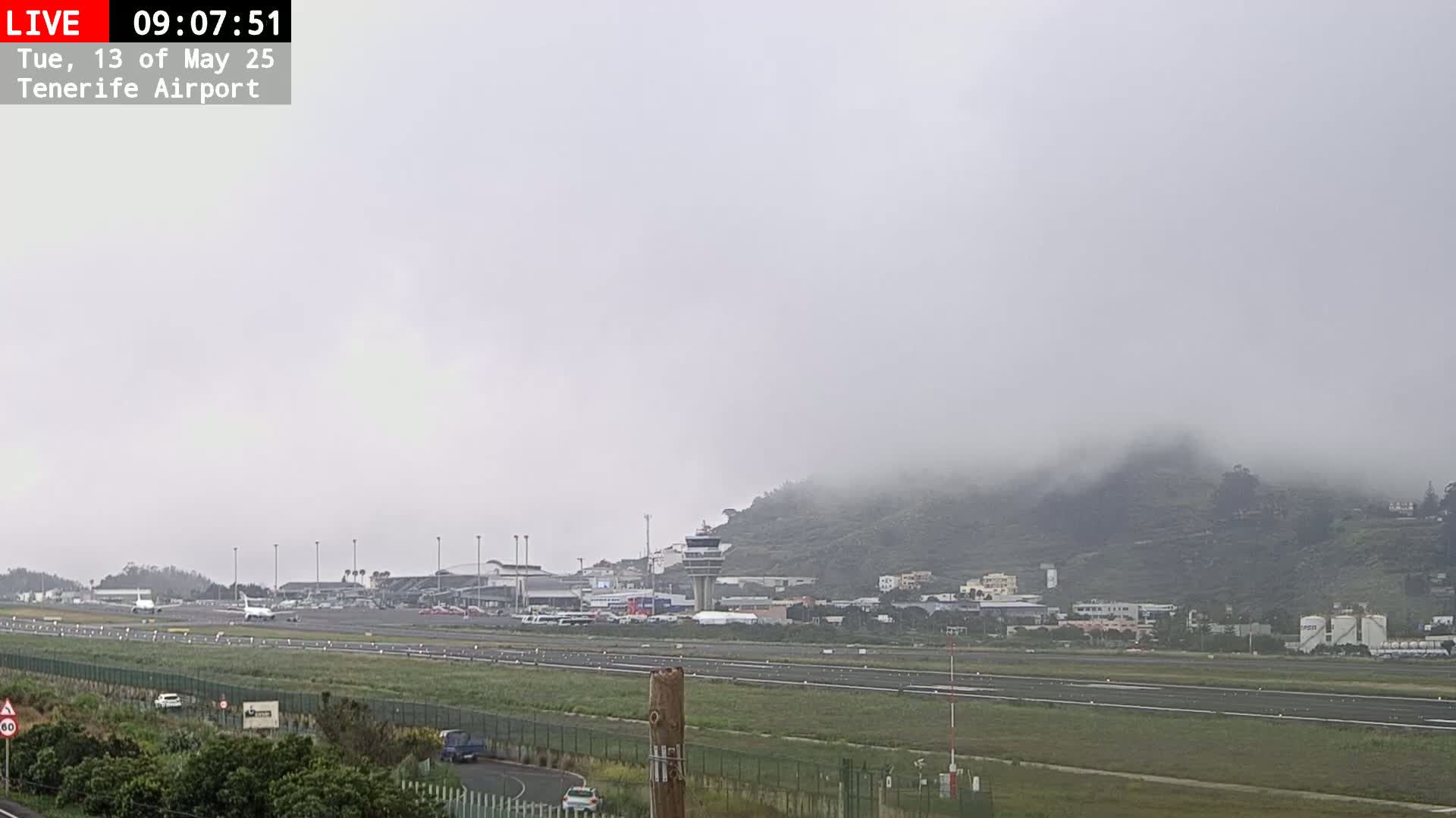 A foggy view of an airport runway, terminal buildings, and a hill shrouded in mist.