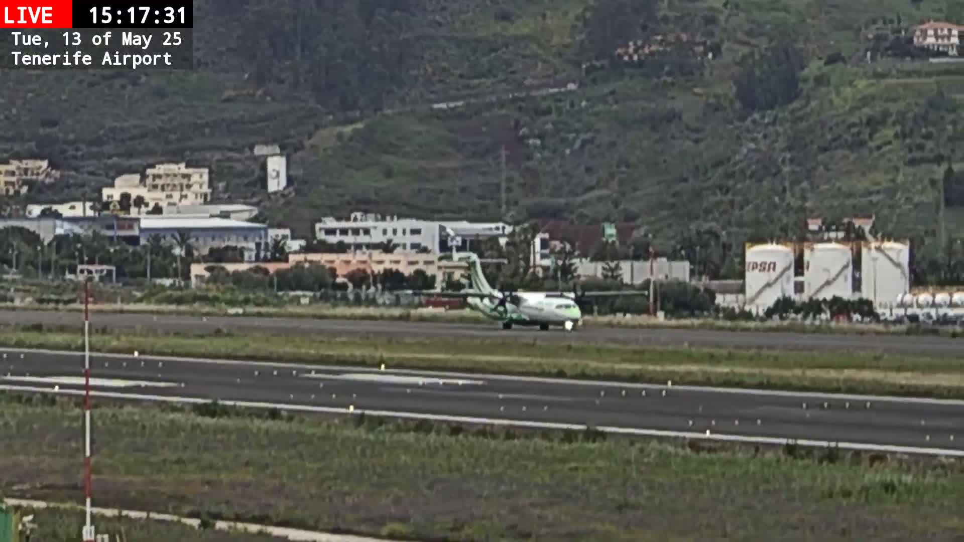 A small passenger plane taxis on a runway near buildings and hills under overcast skies.