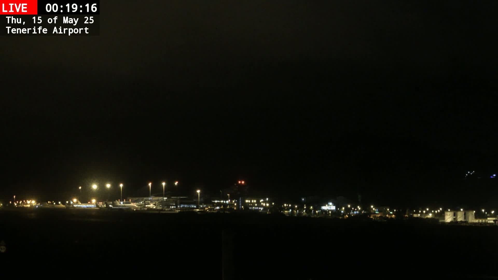 A dark, nighttime view of an airport with dimly lit buildings and runways under an overcast sky.