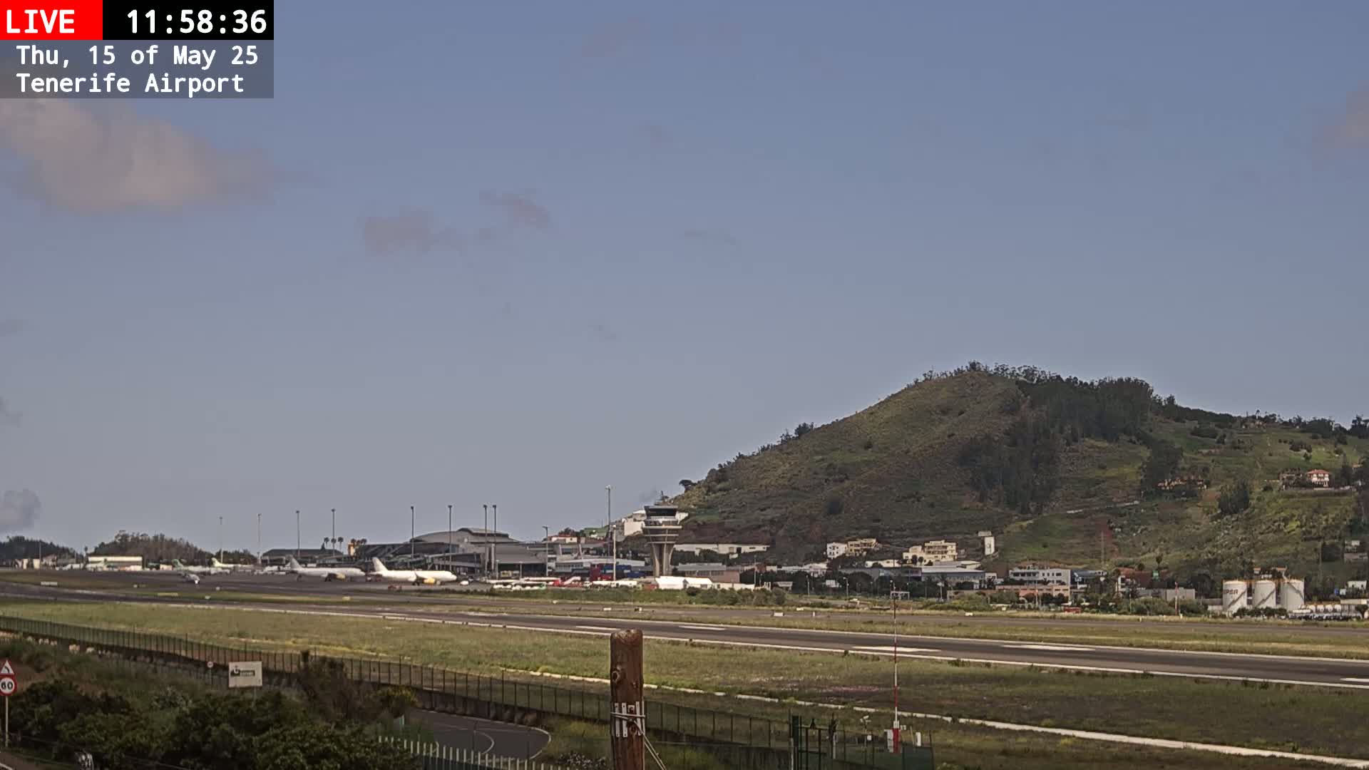 A mostly sunny airport with several airplanes on the tarmac and a green hill in the background.