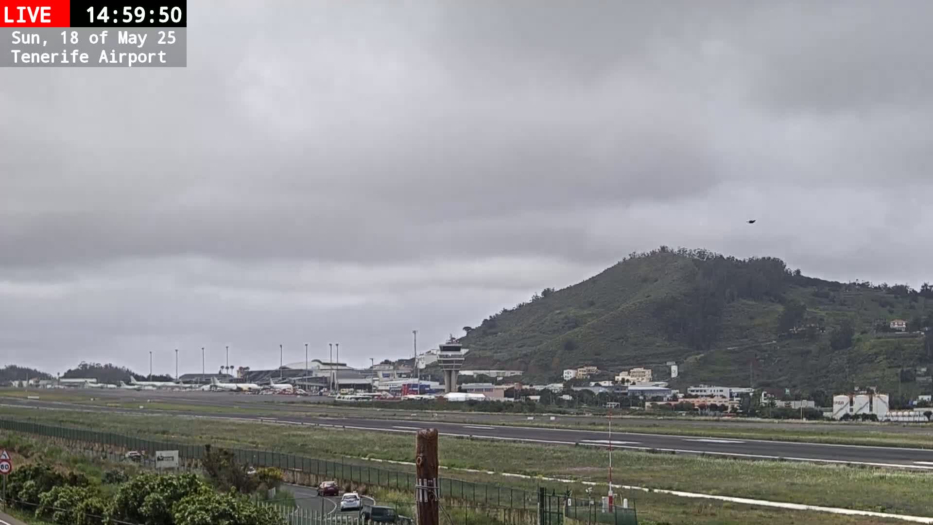 An airport runway with several planes is visible beneath an overcast sky, with a green hill rising in the background.