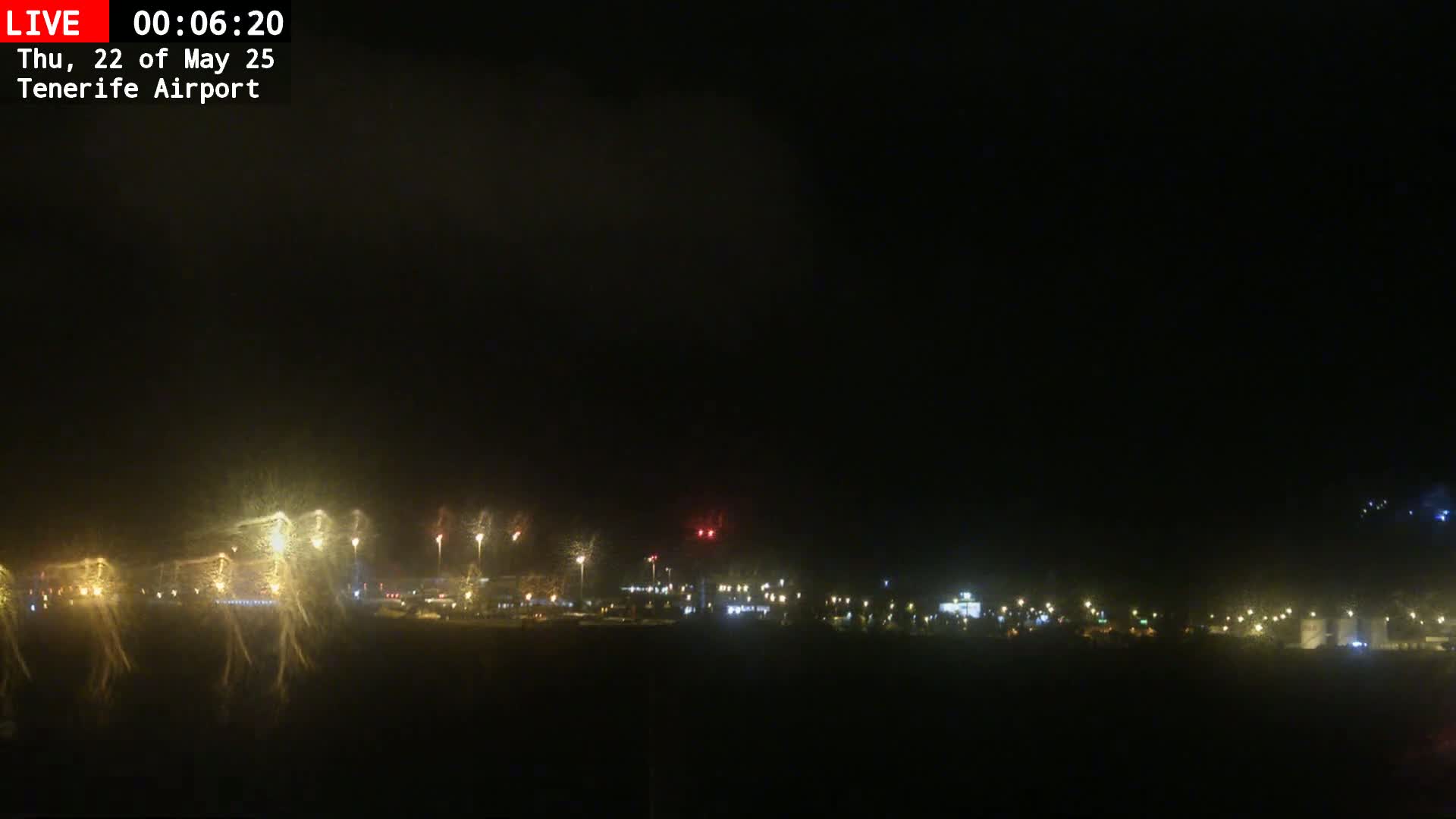 A nighttime view of an airport runway and surrounding buildings illuminated by lights, with a dark, possibly overcast sky.