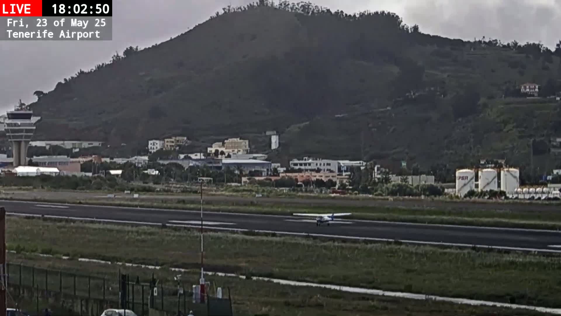 A small airplane taxis on a runway near a hill, under overcast skies.