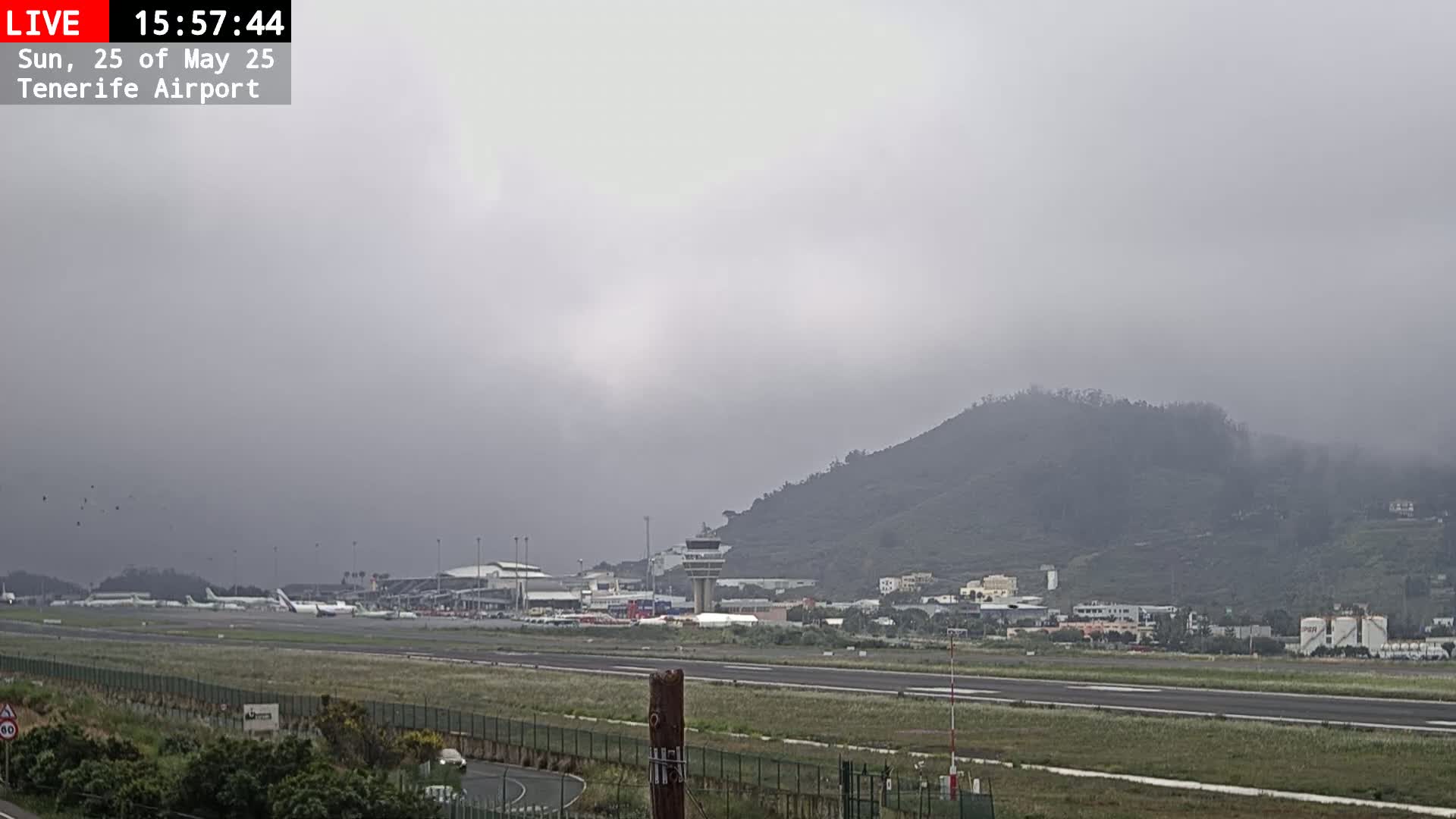 A foggy view of an airport runway, with several planes parked, and a hill in the background.