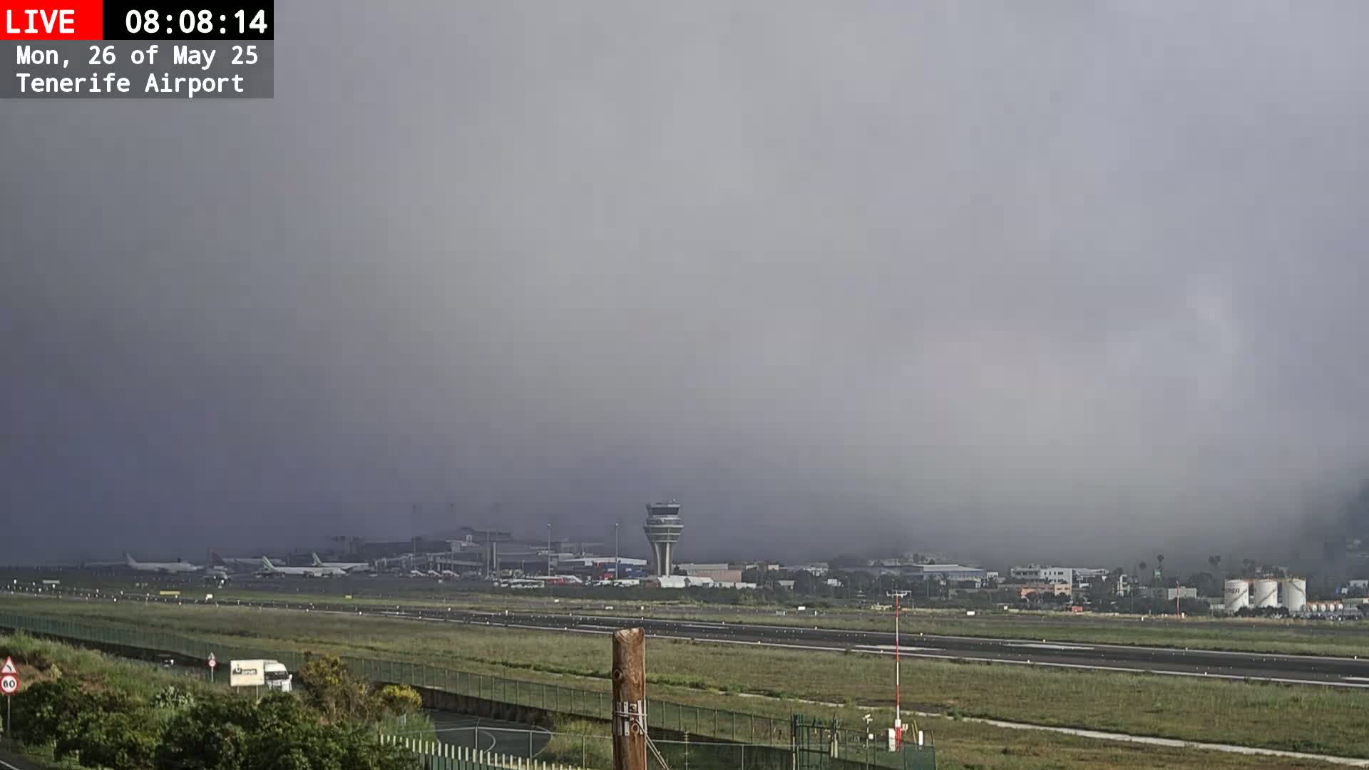 A foggy airport runway with several airplanes and airport buildings visible in the distance.