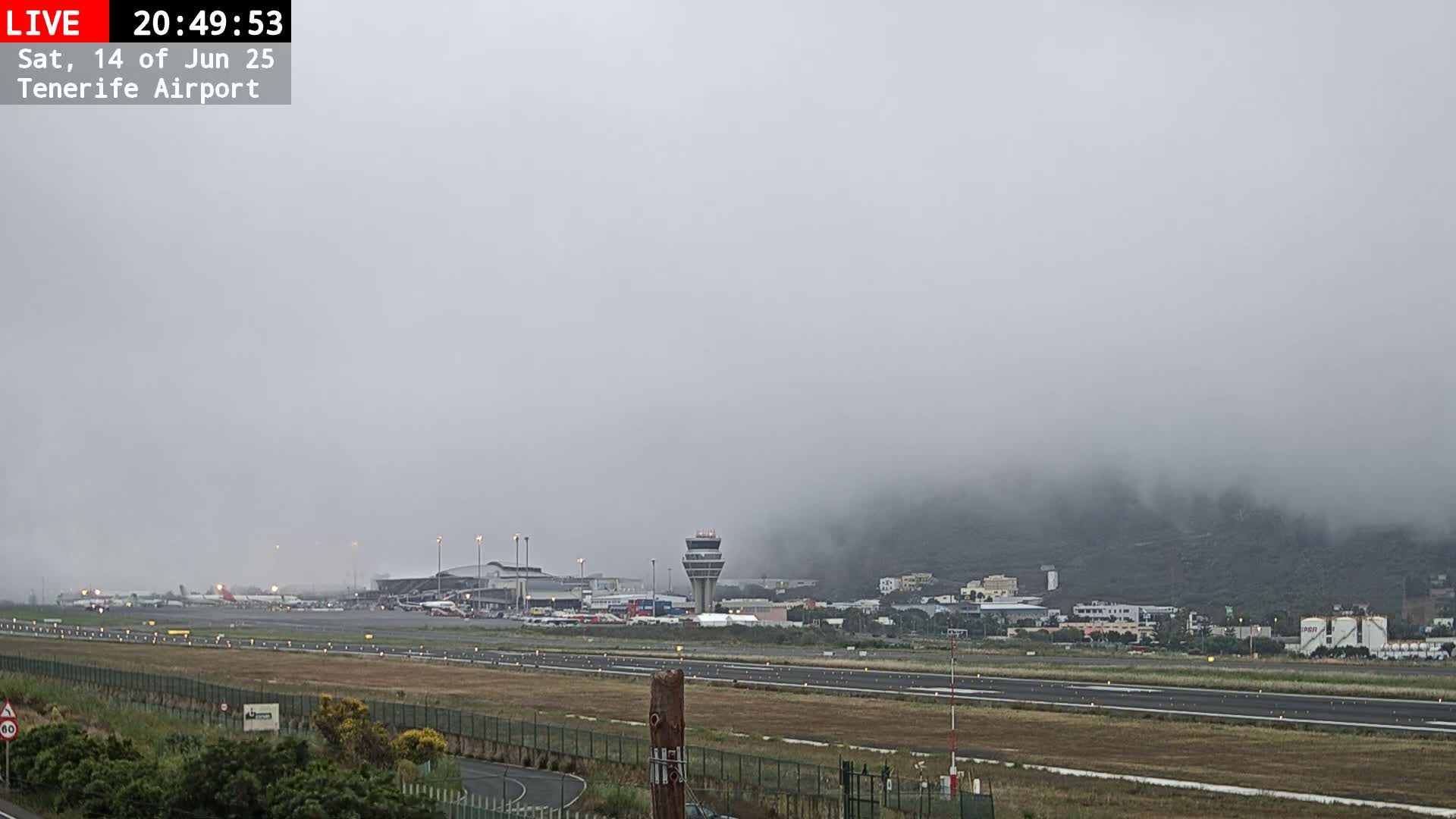A foggy airport runway with several airplanes and airport buildings visible in the distance.