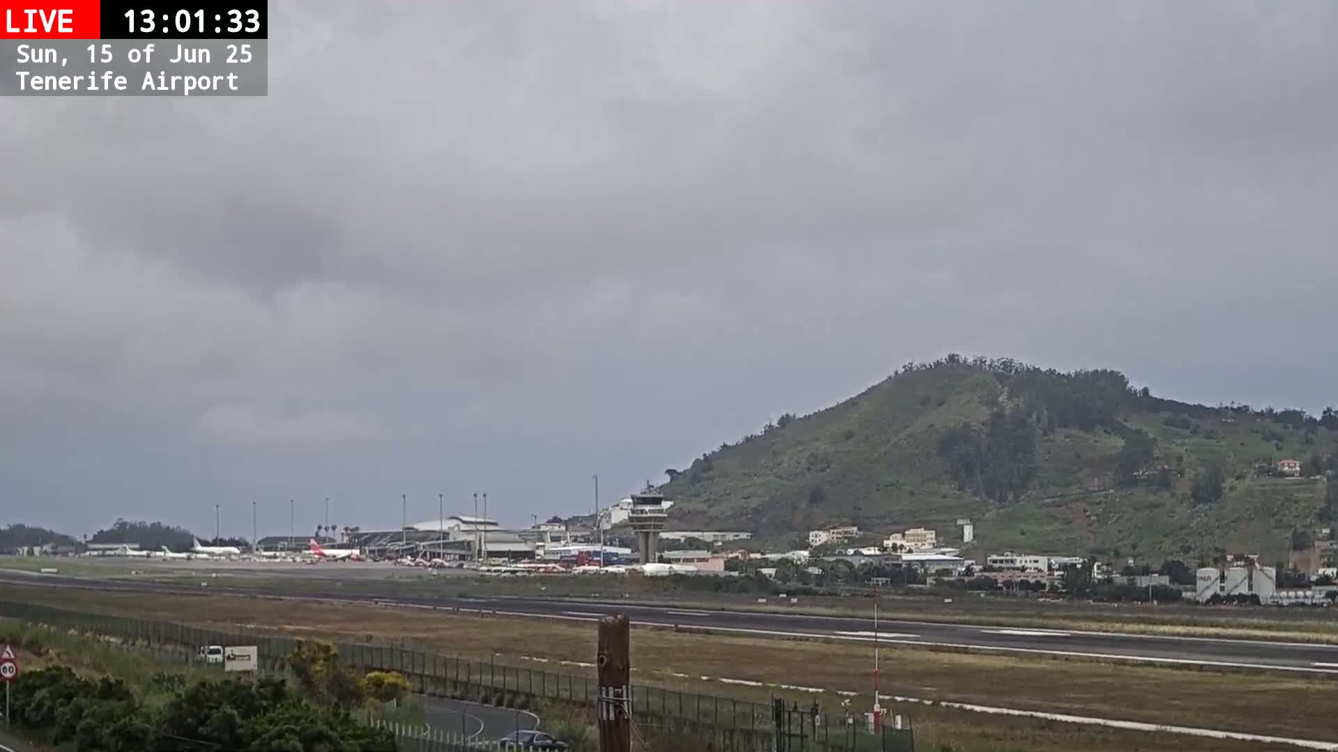 An airport runway with several airplanes is visible under an overcast sky, with a green hill in the background.