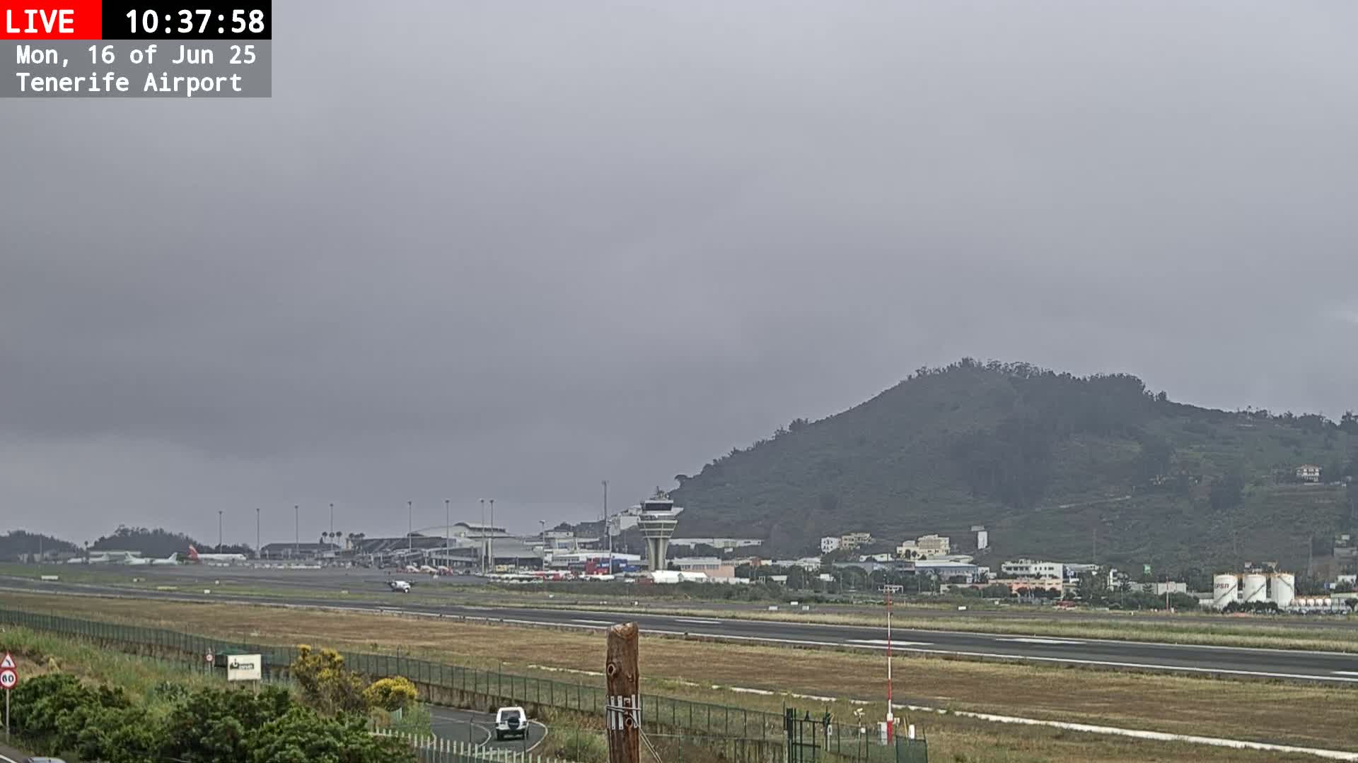 A hazy view of an airport runway, terminal buildings, and a nearby hill under an overcast sky.