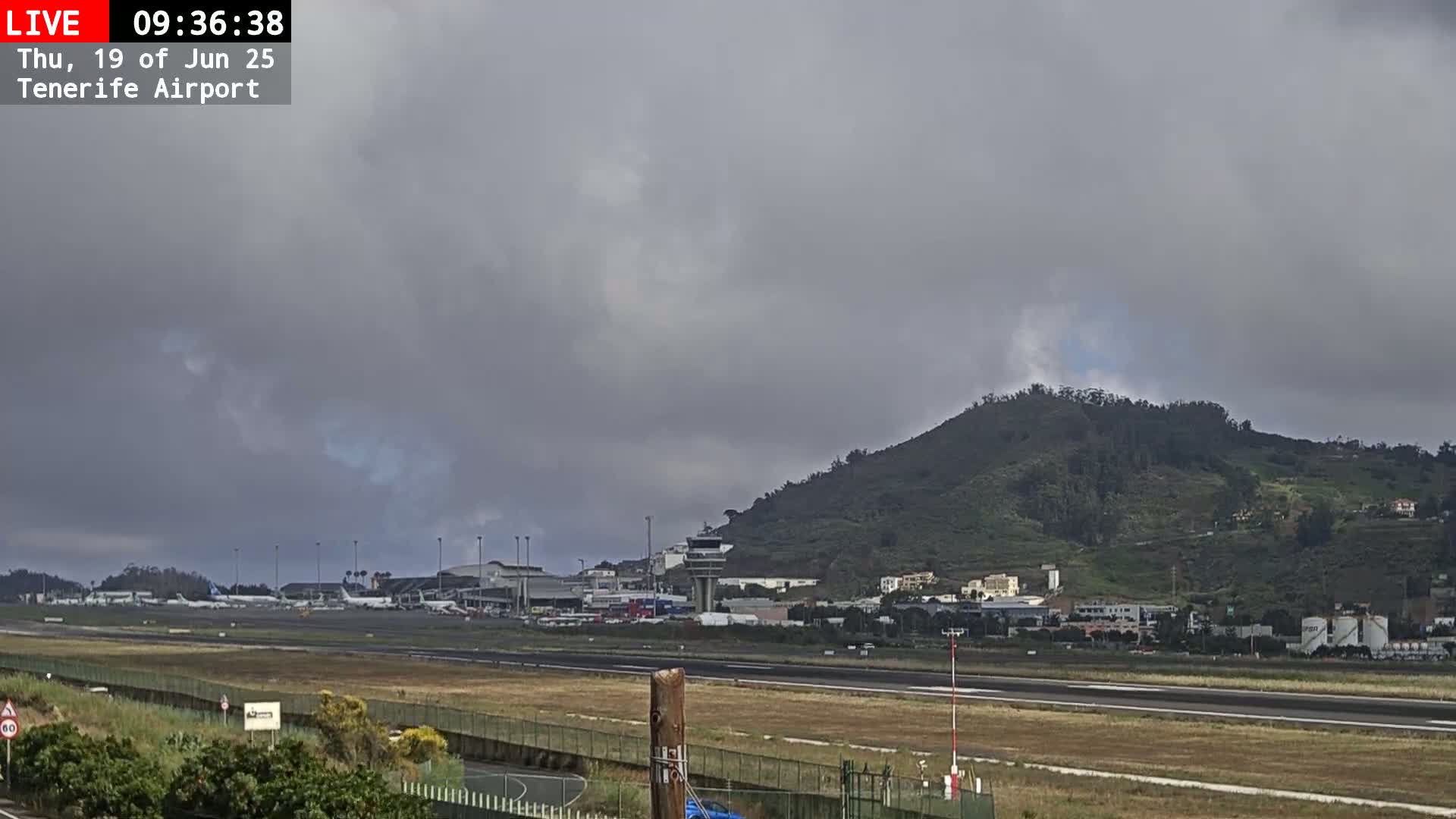 An airport with several airplanes on the tarmac is situated below a hill on an overcast day.