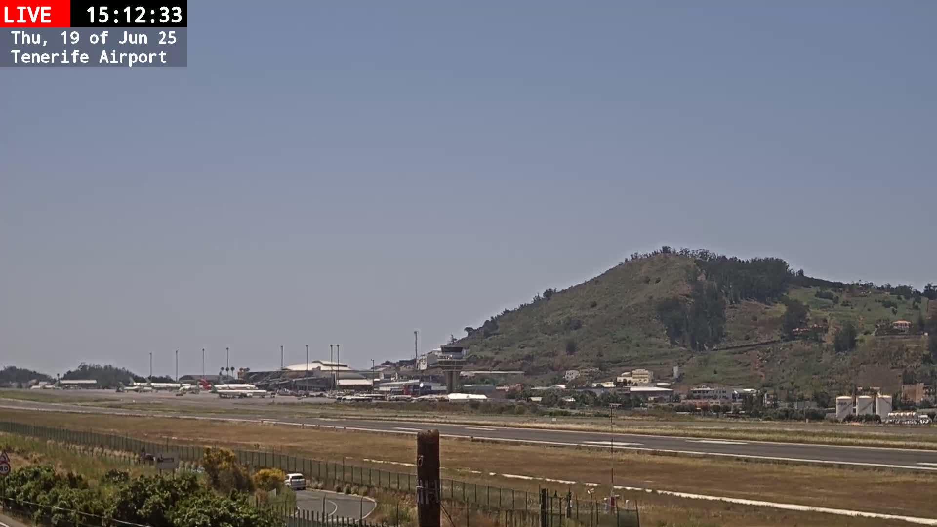 A long runway at an airport stretches toward a green, hilly landscape under a clear sky.