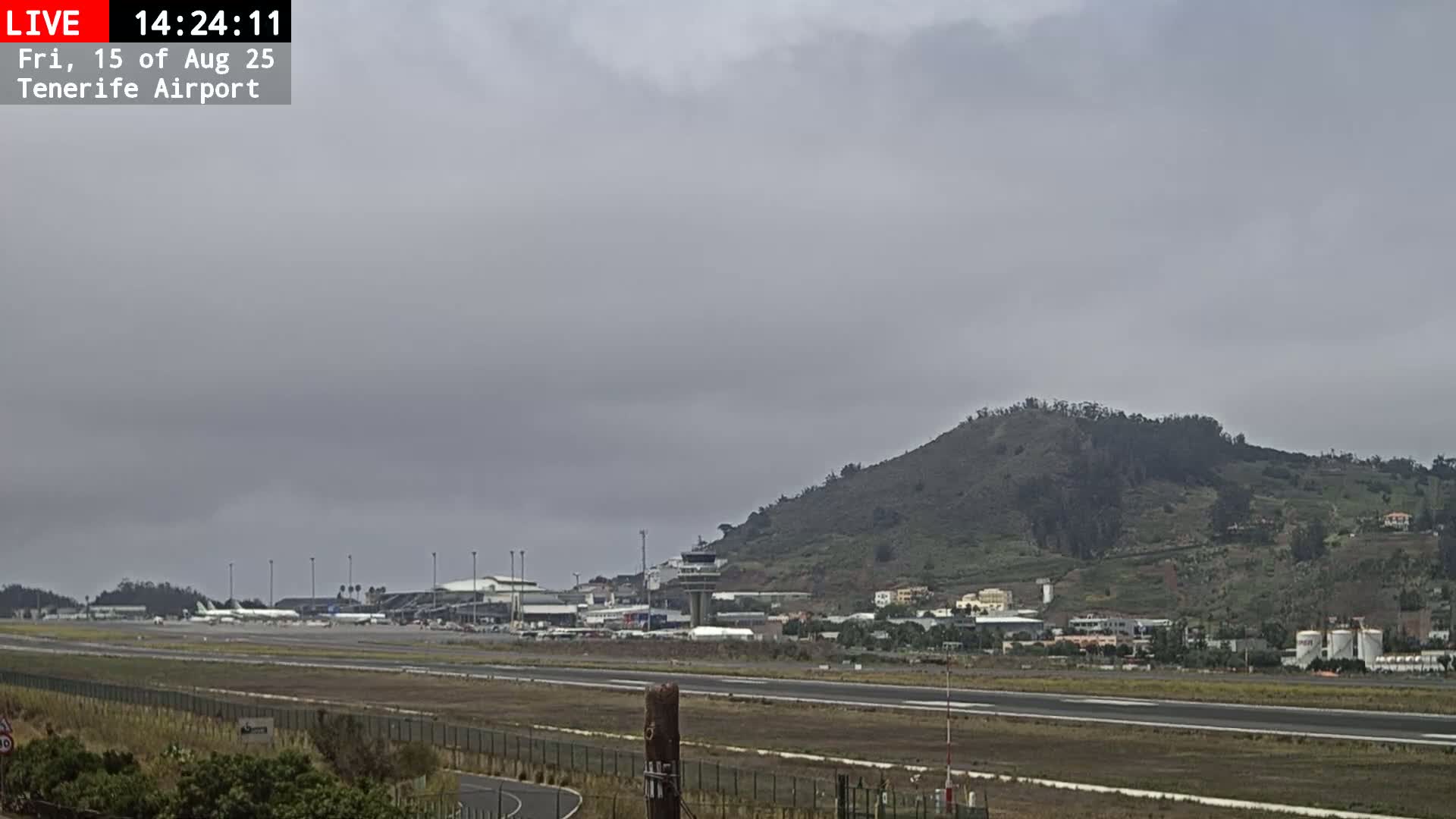 A foggy view of an airport runway, terminal buildings, and airplanes, with a hill shrouded in mist in the background.