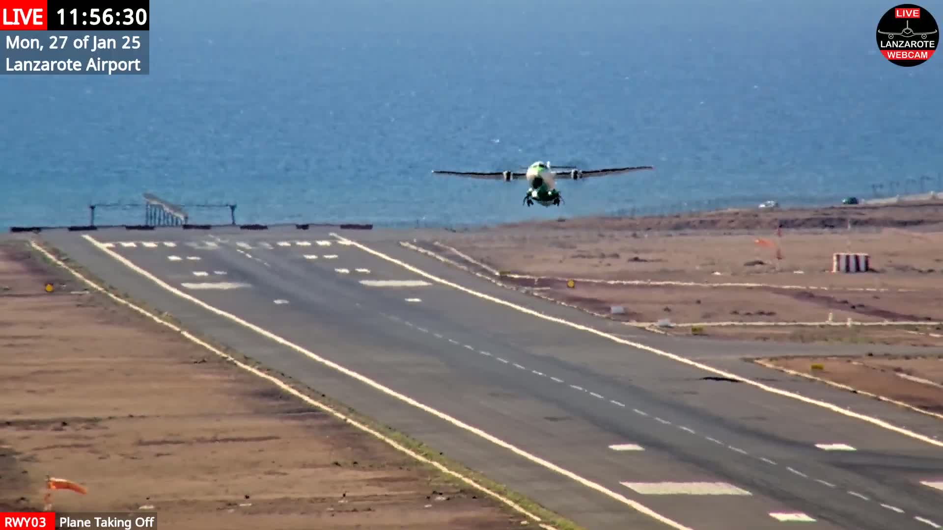 A small plane is taking off from an airport runway next to a body of water on a clear day.