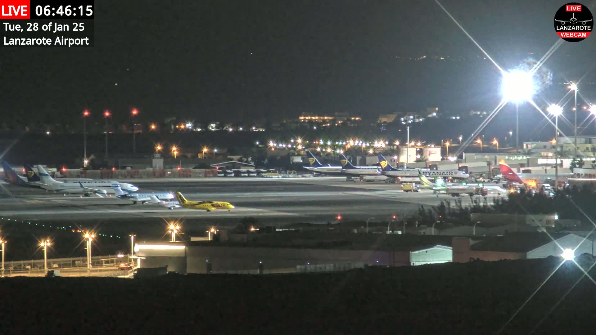 At night, several airplanes are parked on a brightly lit airport tarmac.