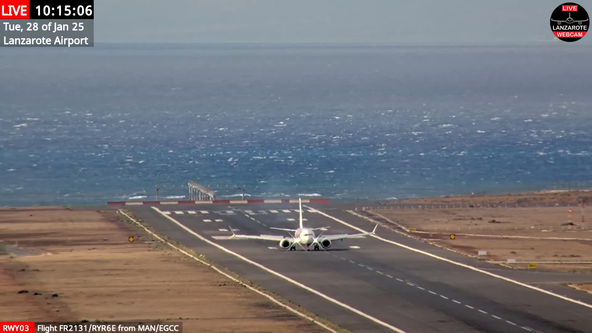 A commercial airplane is landing on a runway next to a windy ocean.