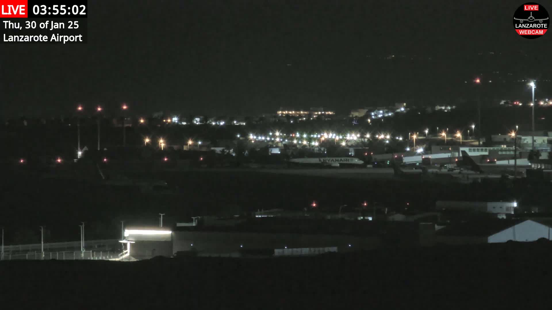 A nighttime view of an airport with several illuminated buildings and a plane on the tarmac under a clear, dark sky.