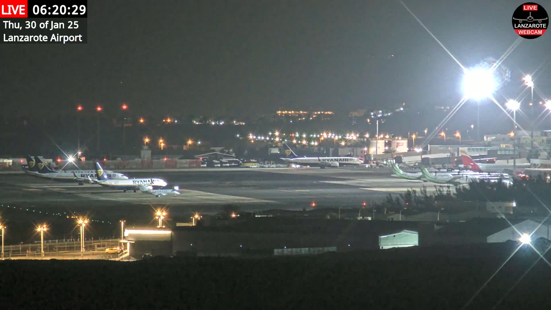 A nighttime view of an airport tarmac with several airplanes parked and illuminated by bright lights.