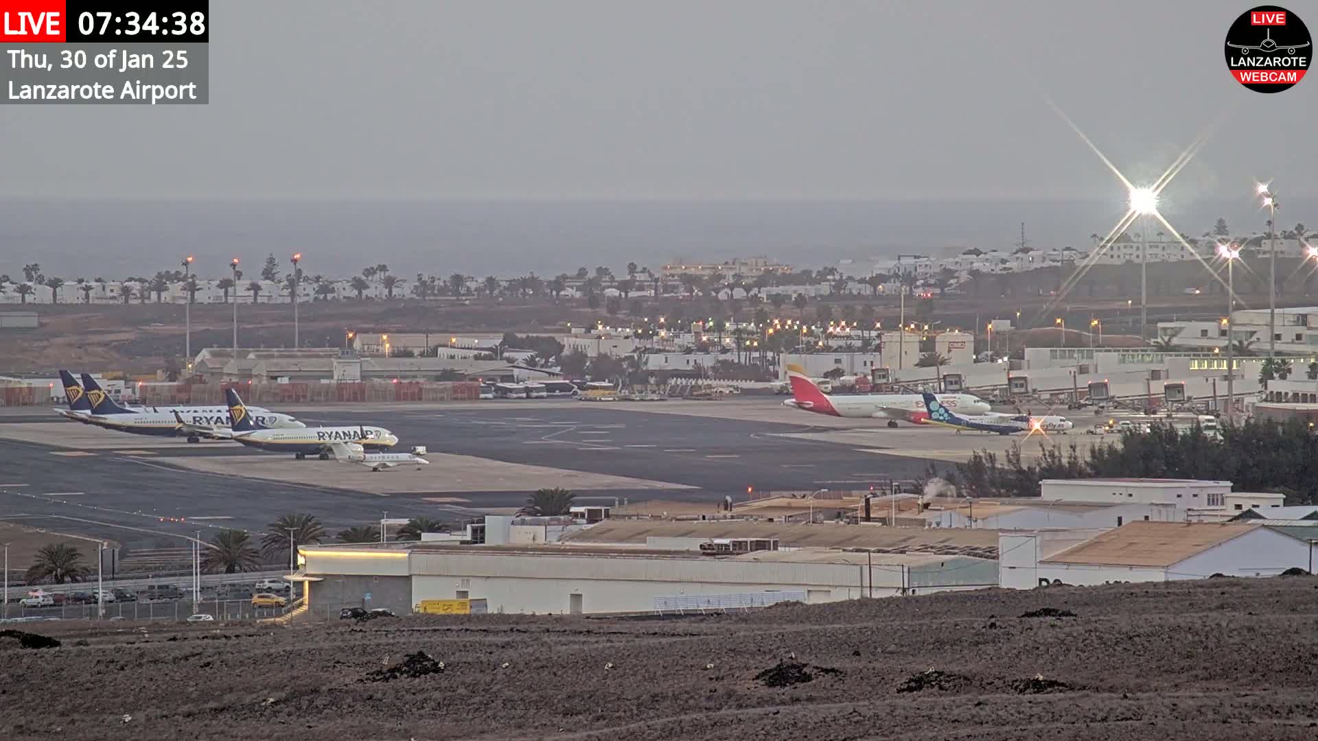 Several airplanes are parked on a tarmac at an airport near a body of water under an overcast sky.