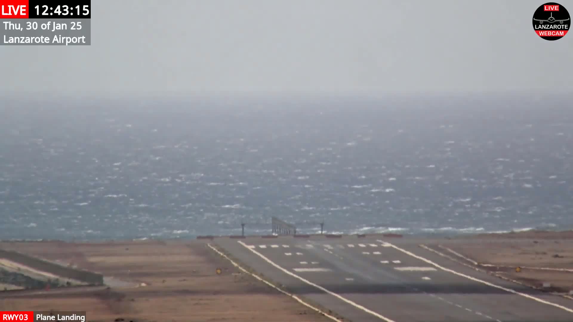 A windy, hazy day is shown at an airport runway overlooking a choppy ocean.