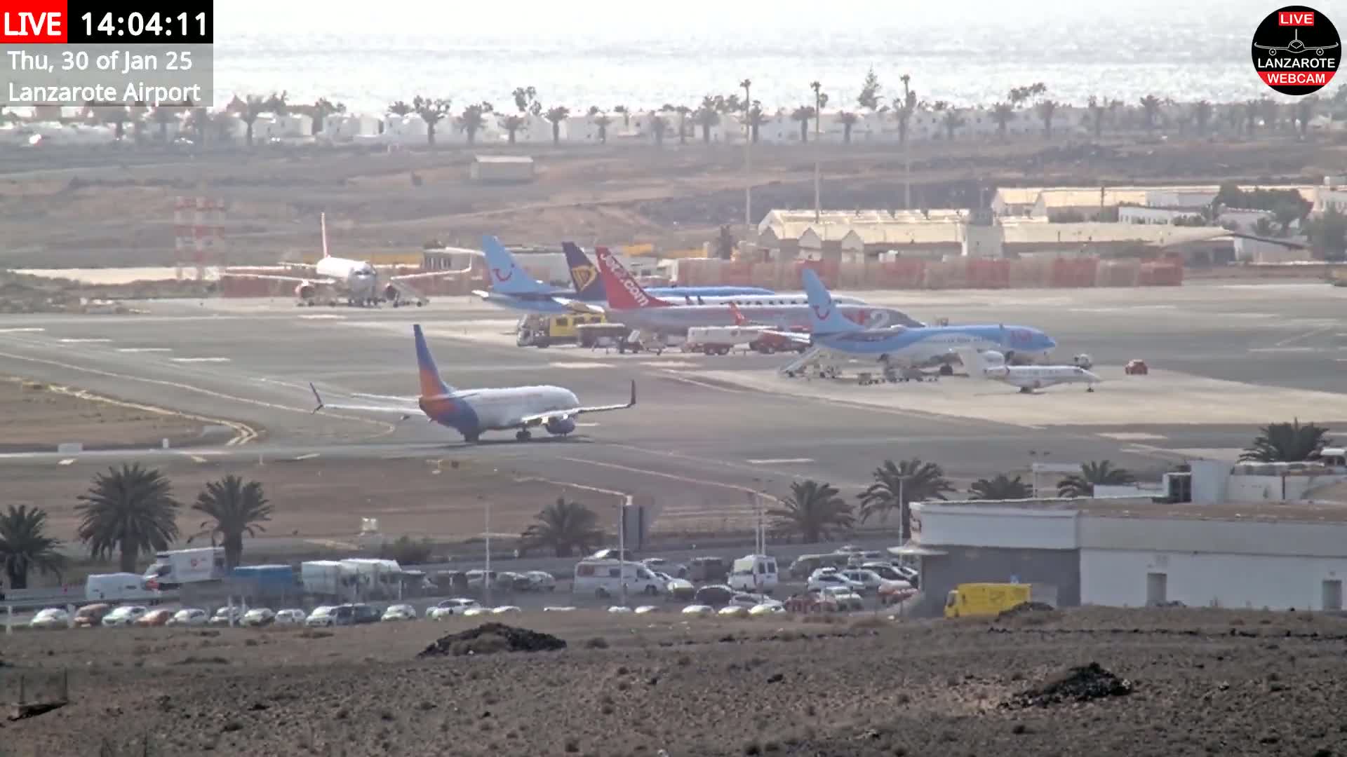 Several airplanes are parked on an airport tarmac on a hazy day with a calm ocean visible in the distance.