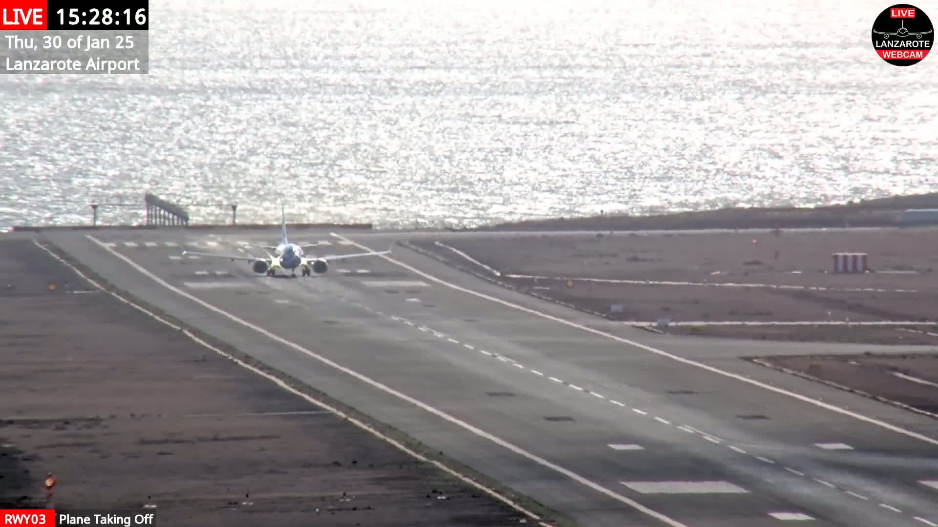A passenger plane is taking off from a runway next to a body of water under sunny conditions.