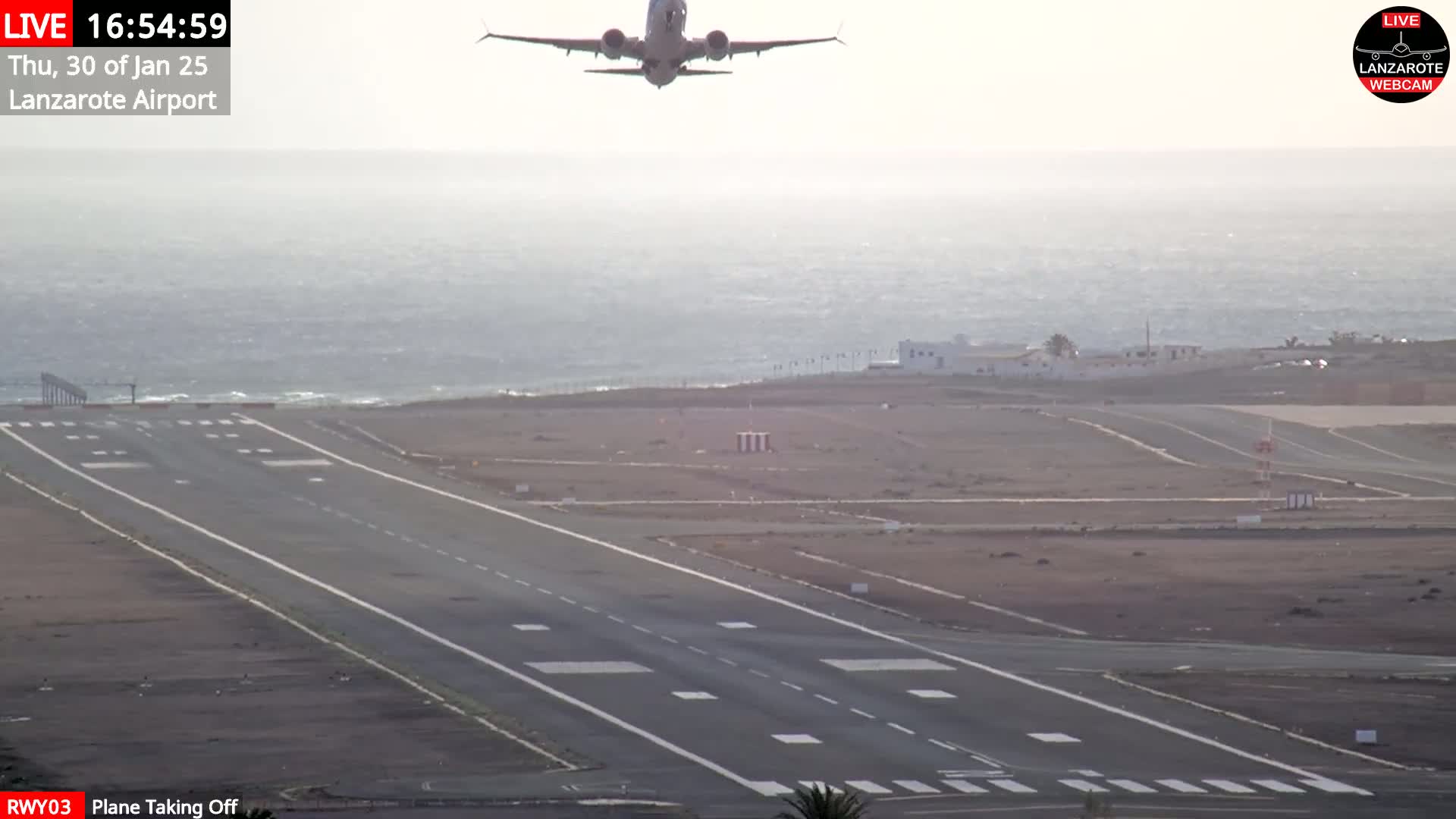 A plane is taking off from an airport runway next to a body of water under hazy conditions.