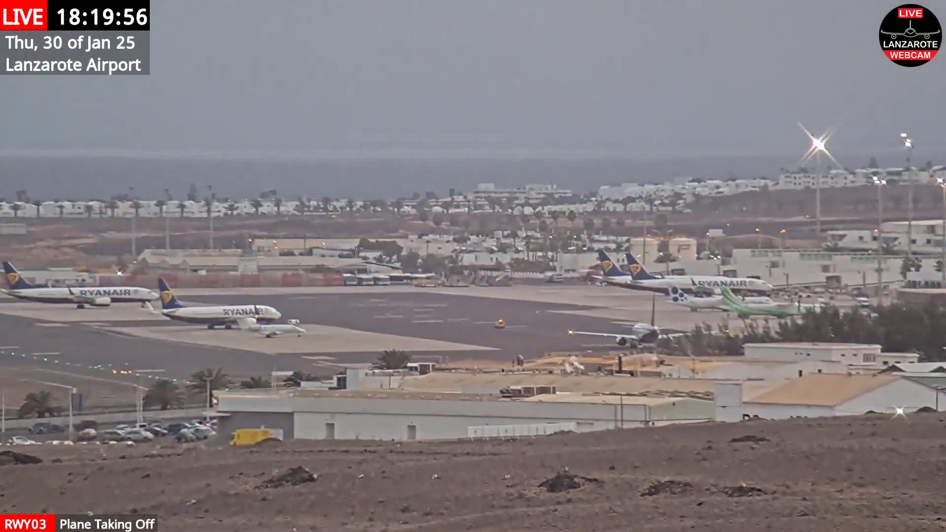 Several airplanes are parked on an airport tarmac on an overcast day, with an ocean visible in the distance.