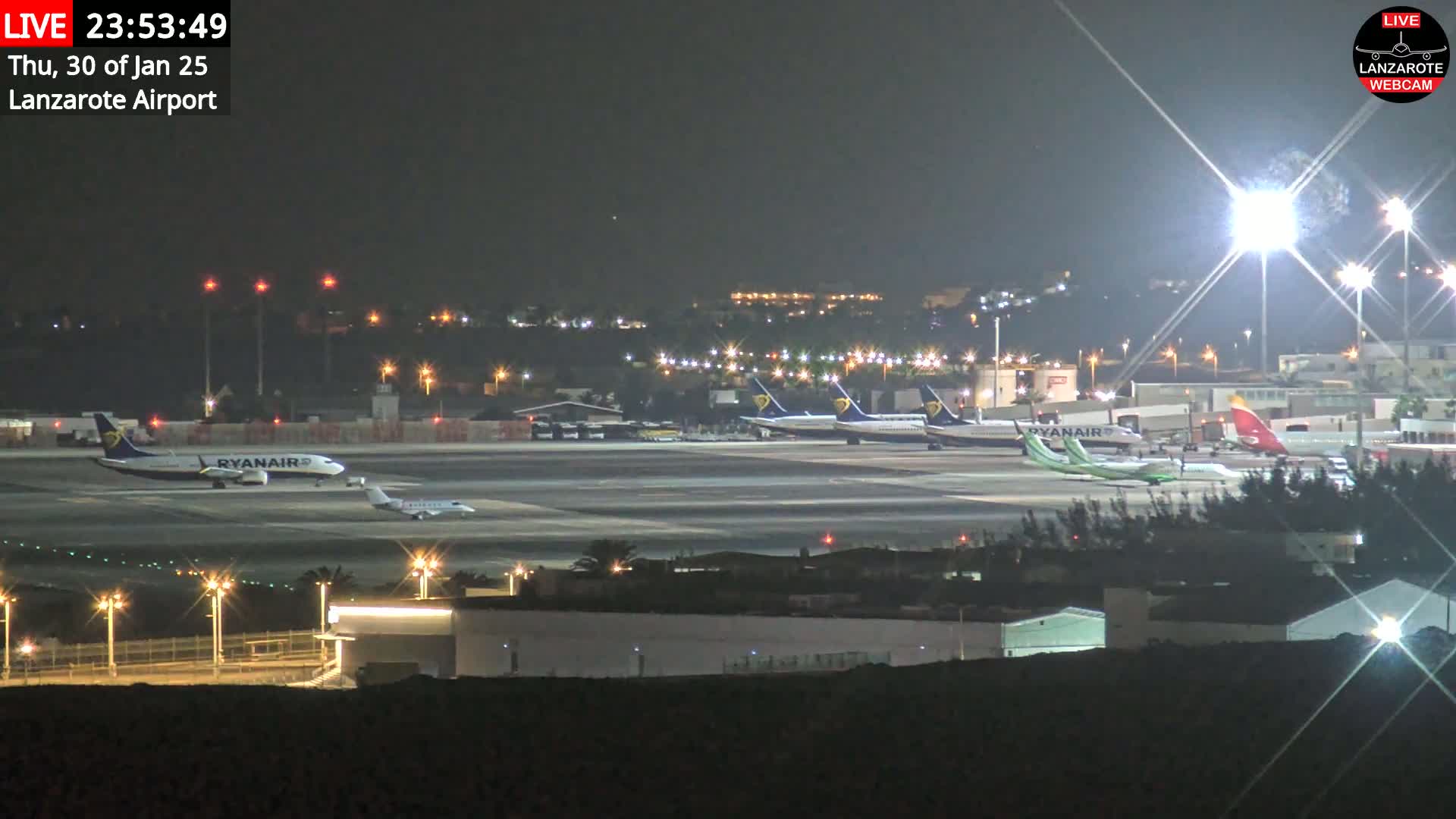 Several airplanes are parked on a brightly lit airport tarmac at night.