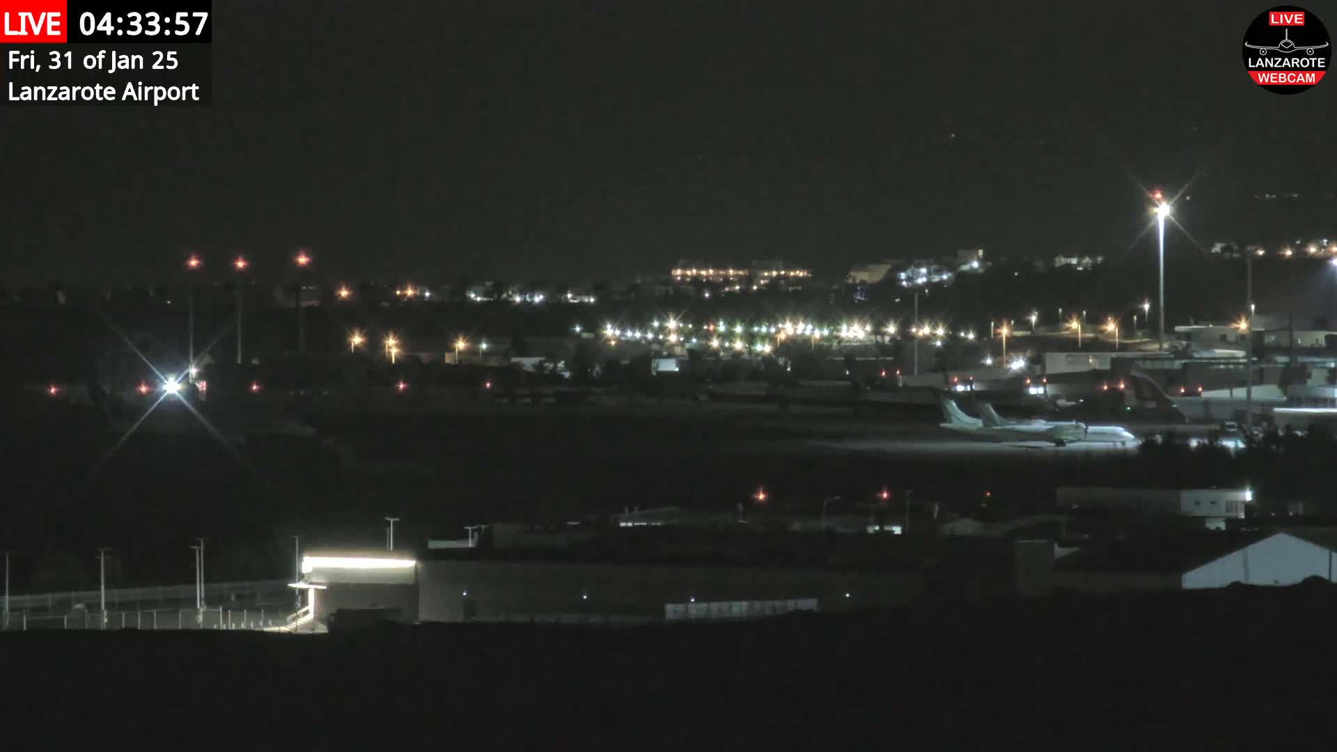 A nighttime view of an airport with a plane on the tarmac and numerous lights illuminating the surrounding buildings and landscape under a clear, dark sky.