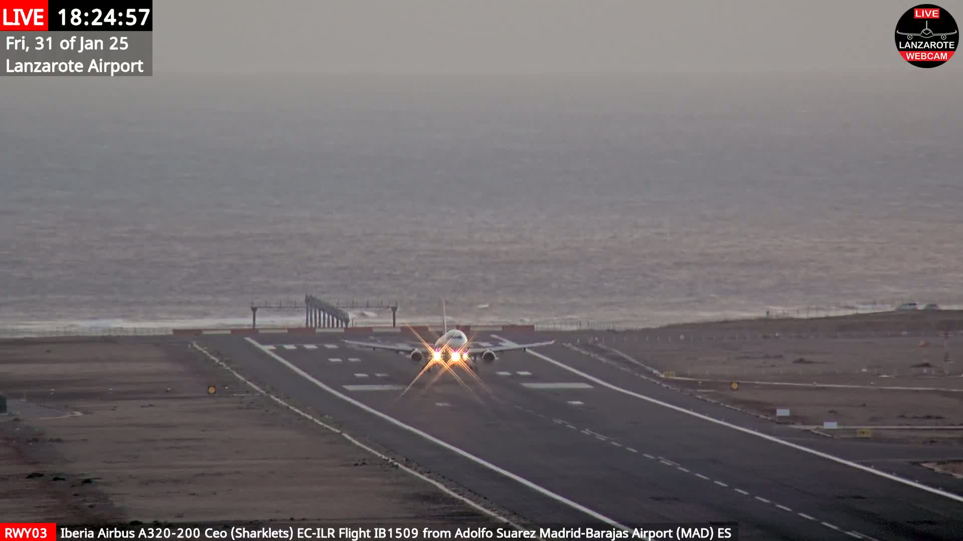 An airplane is landing on a runway next to a body of water under overcast skies.