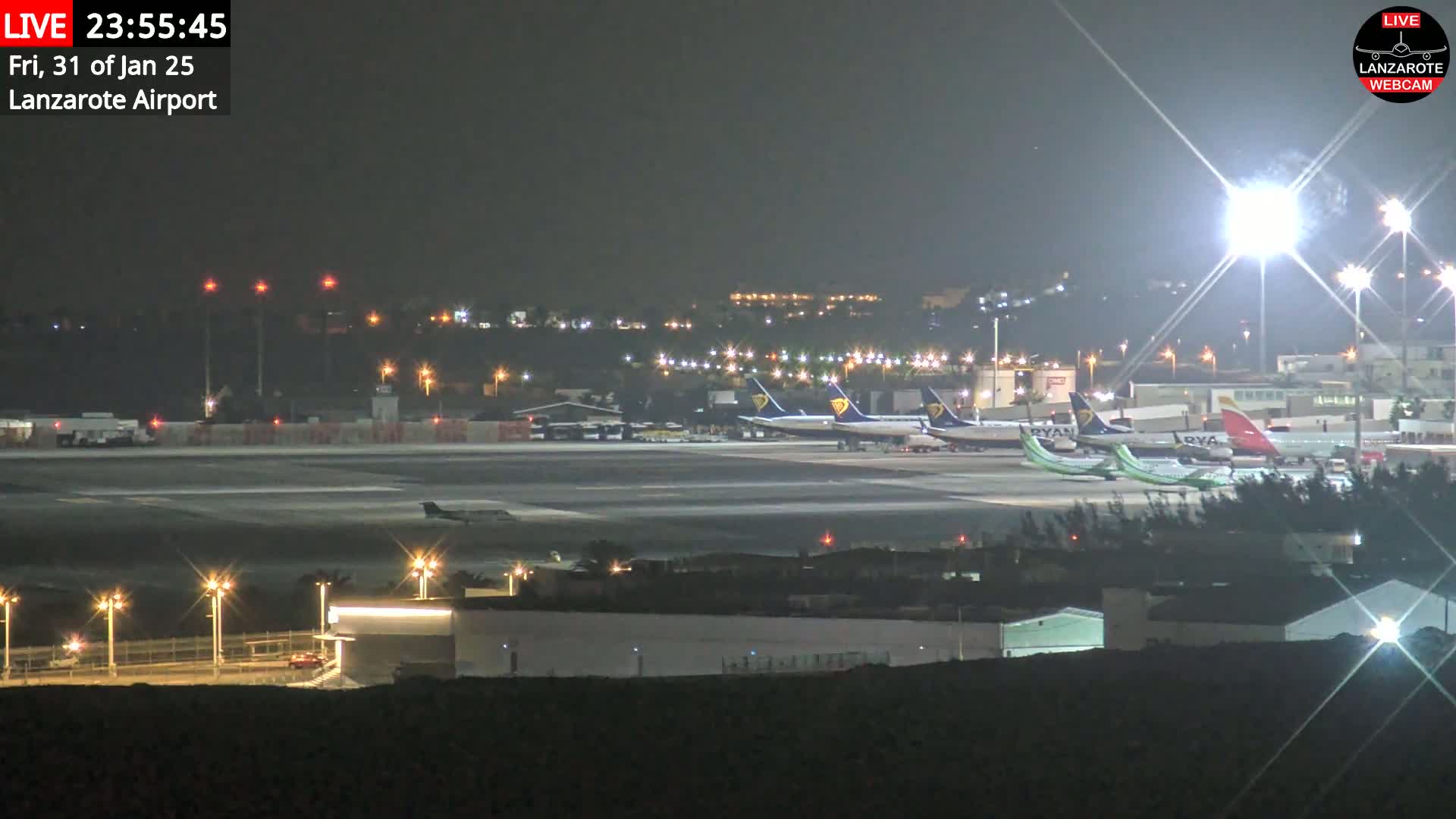 A nighttime view of an airport tarmac with several airplanes parked, illuminated by bright lights under a dark, clear sky.