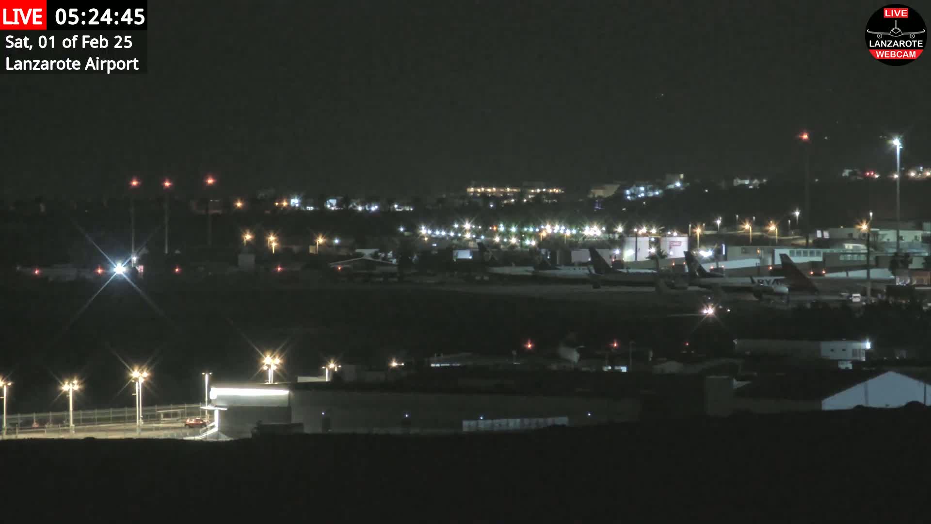 A nighttime view of an airport with several airplanes parked on the tarmac under a clear, dark sky.