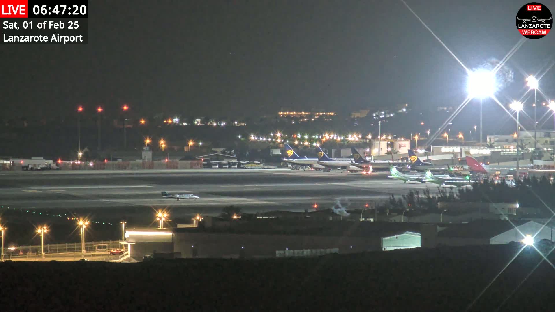 A nighttime view of an airport tarmac with several airplanes parked, illuminated by bright lights under a clear sky.