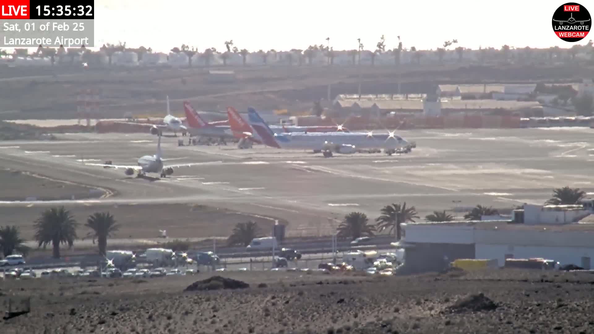 Several airplanes are parked on a tarmac at an airport on a hazy, sunny day.