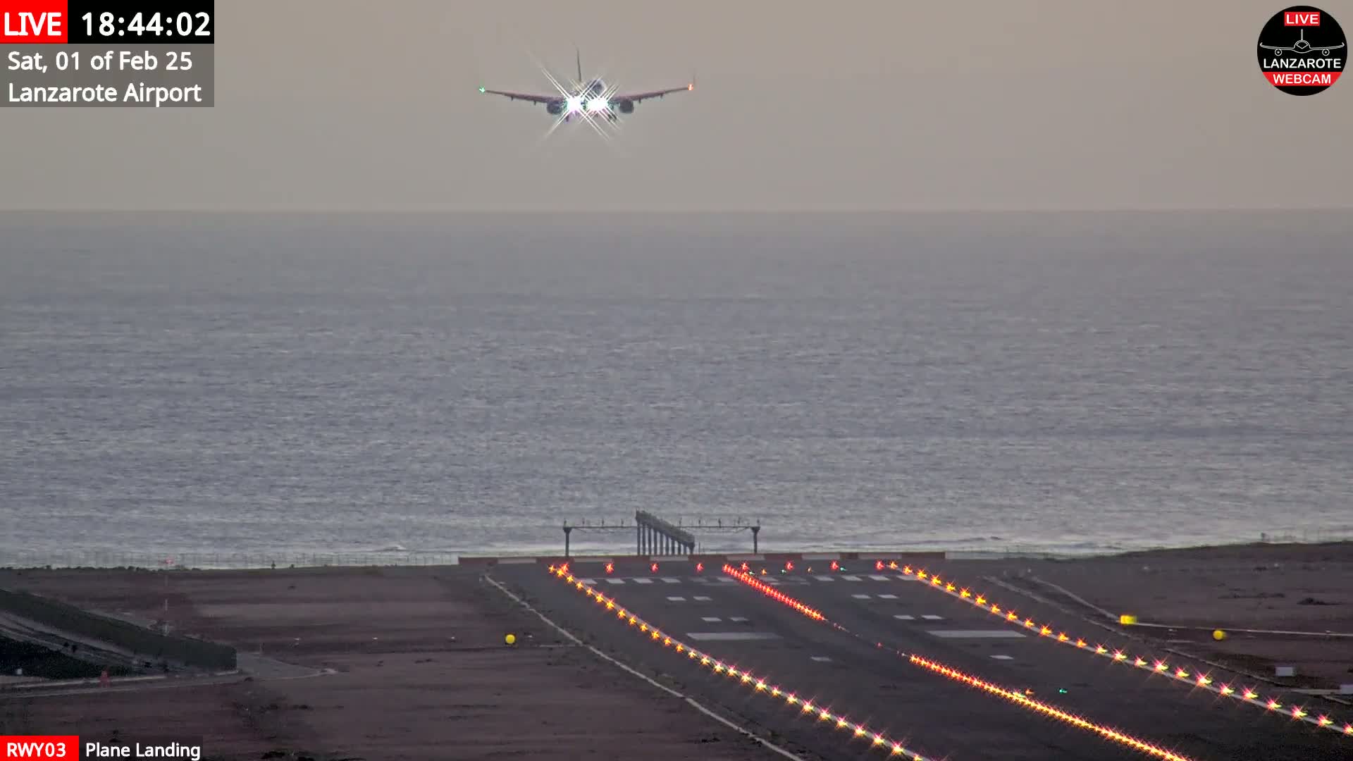 A plane is landing on a runway next to a body of water under an overcast sky.