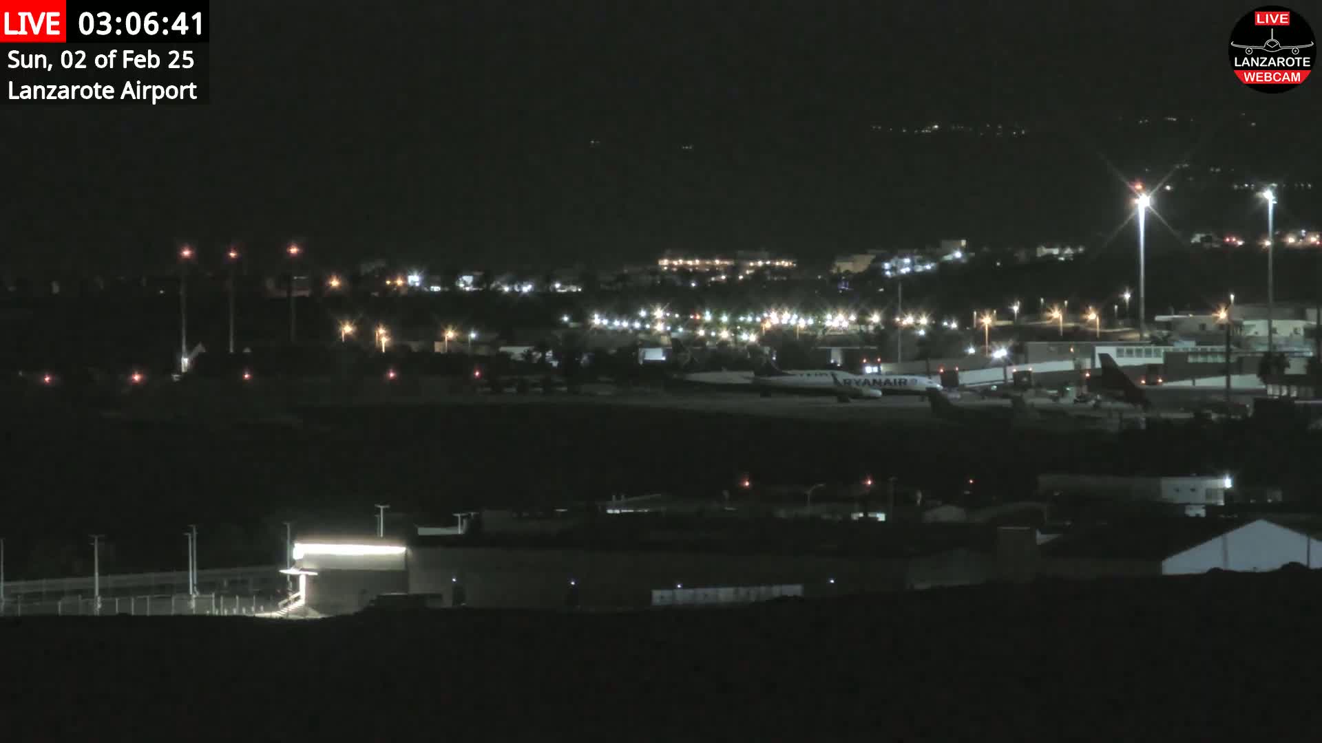 A nighttime view of an airport with a Ryanair plane on the tarmac under a clear, dark sky.