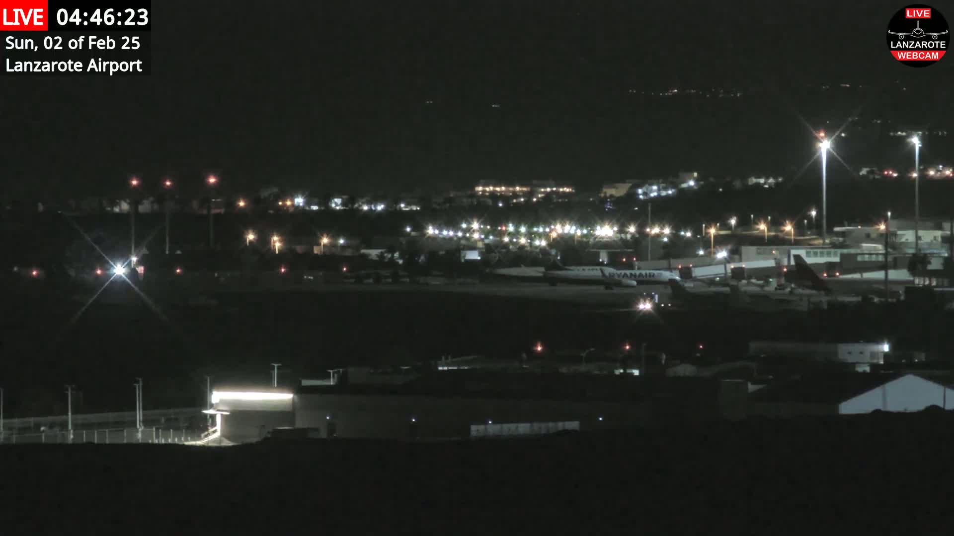 A nighttime view of an airport with several lights illuminating planes and buildings under a clear, dark sky.