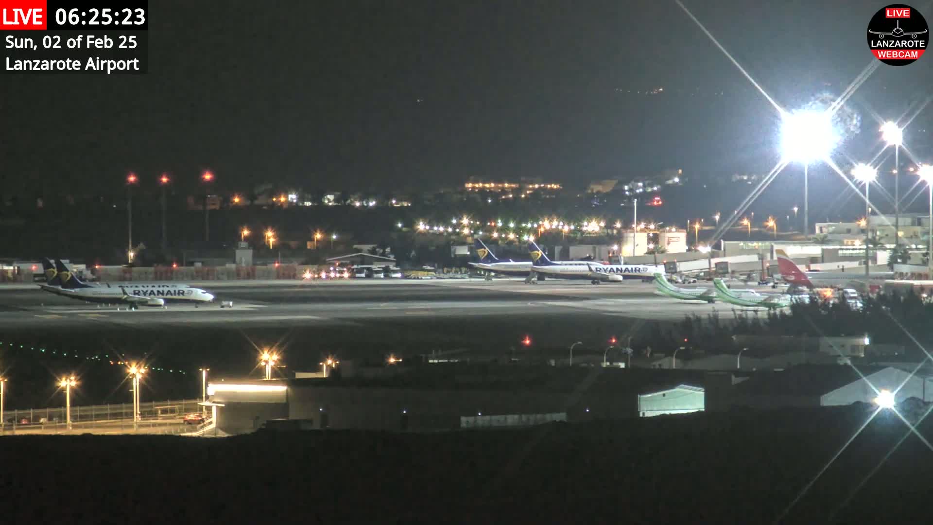 At night, several airplanes are parked on a brightly lit airport tarmac.
